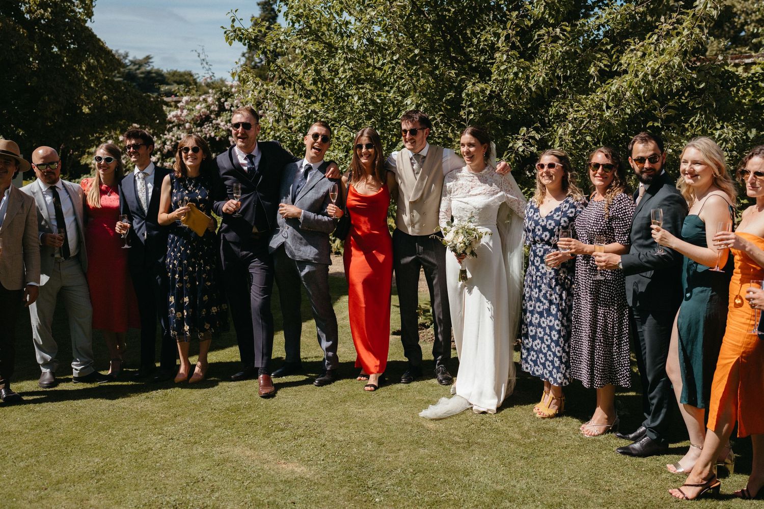 Large group of wedding guests gather on a sunny lawn for photographs.