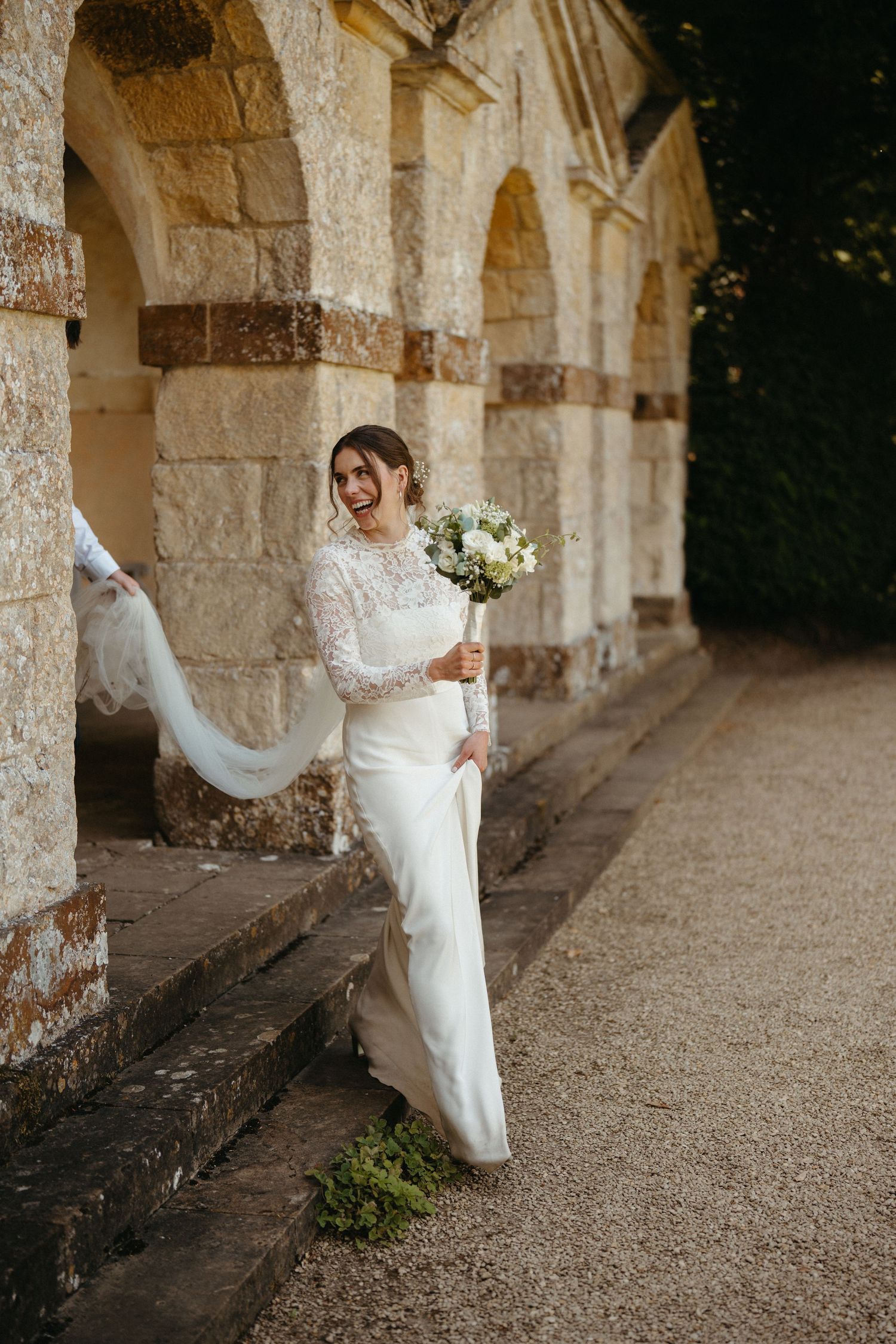 A bride in flowing white dress twirls gracefully under historic stone arches.