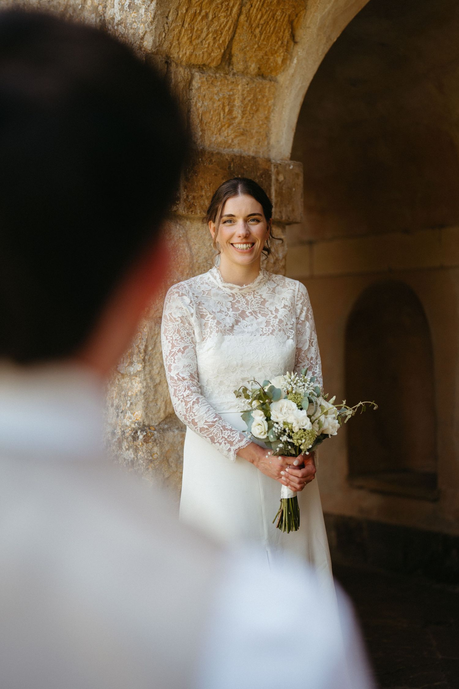 A stunning wedding portrait captured under a stone archway with natural lighting.