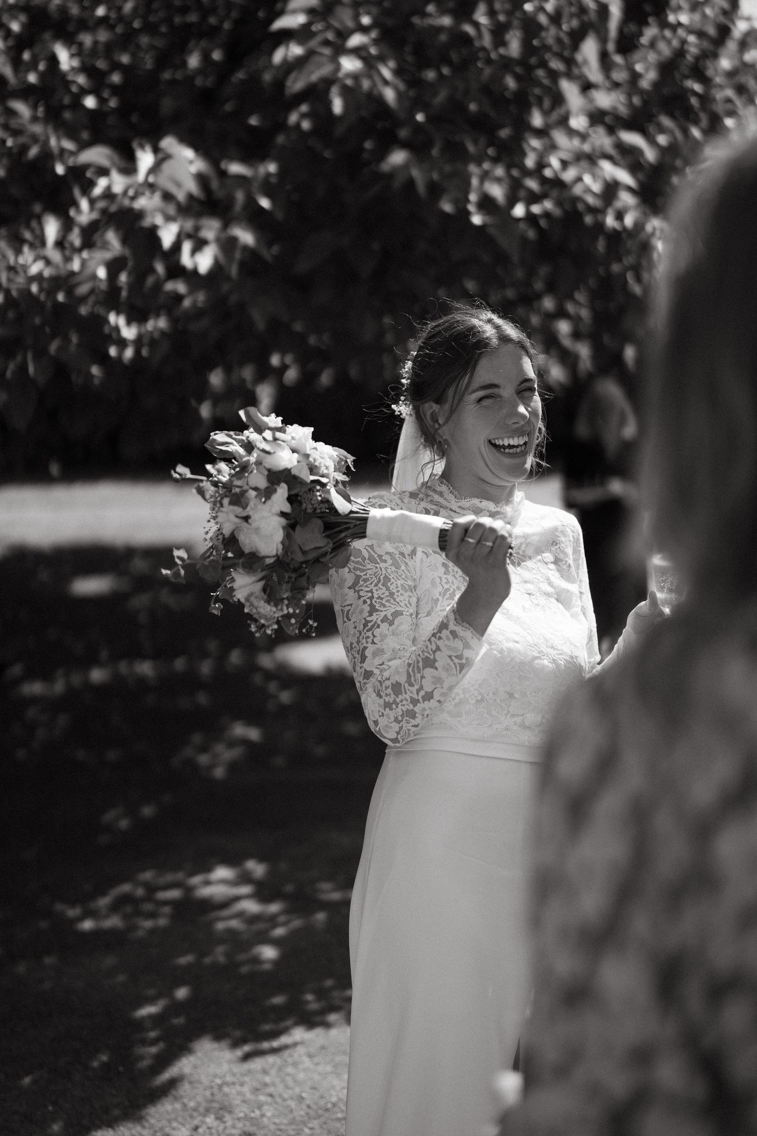 Black and white portrait of a bride in lace dress smiling outdoors.
