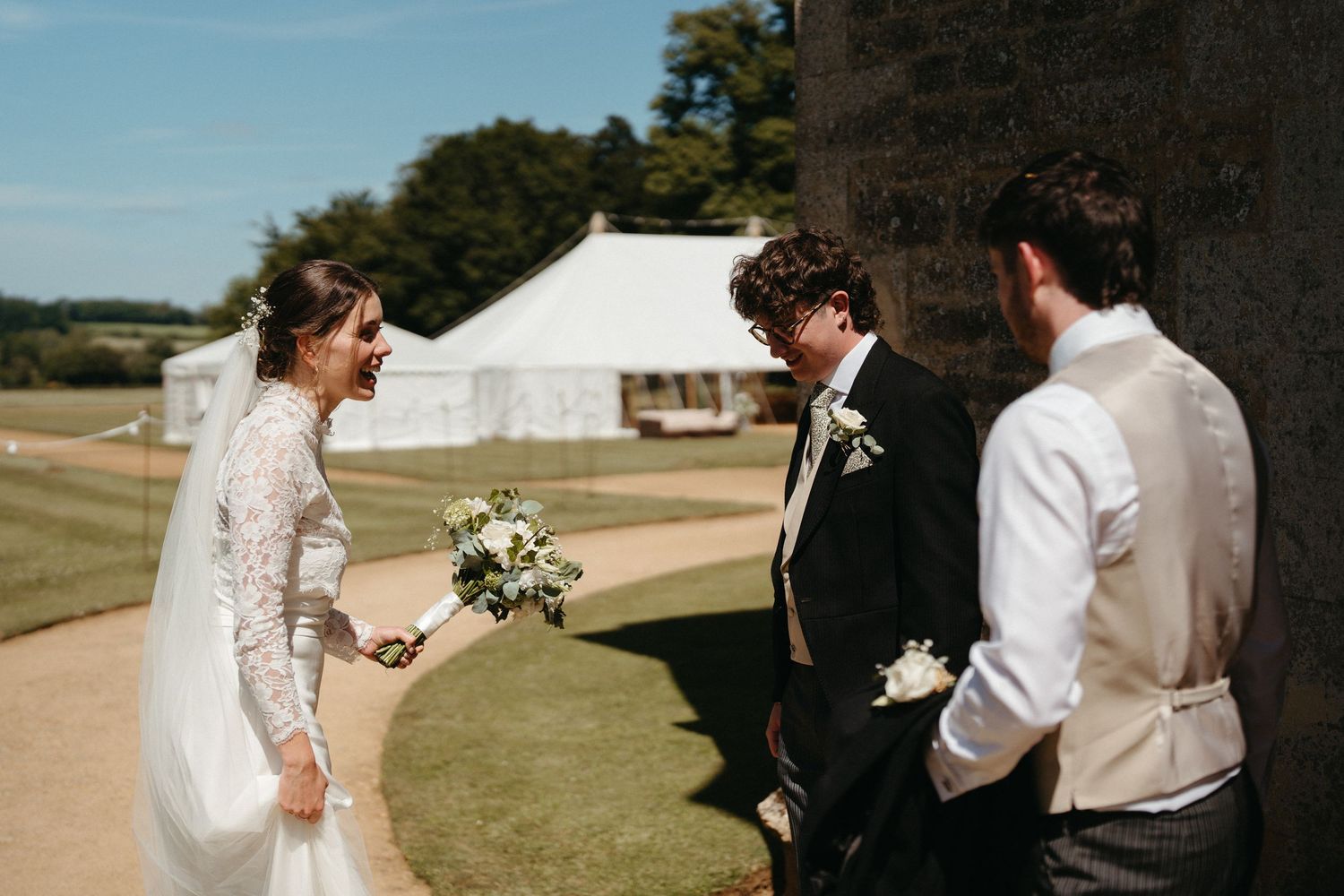 A wedding party celebrates in a rustic outdoor setting on a sunny afternoon.