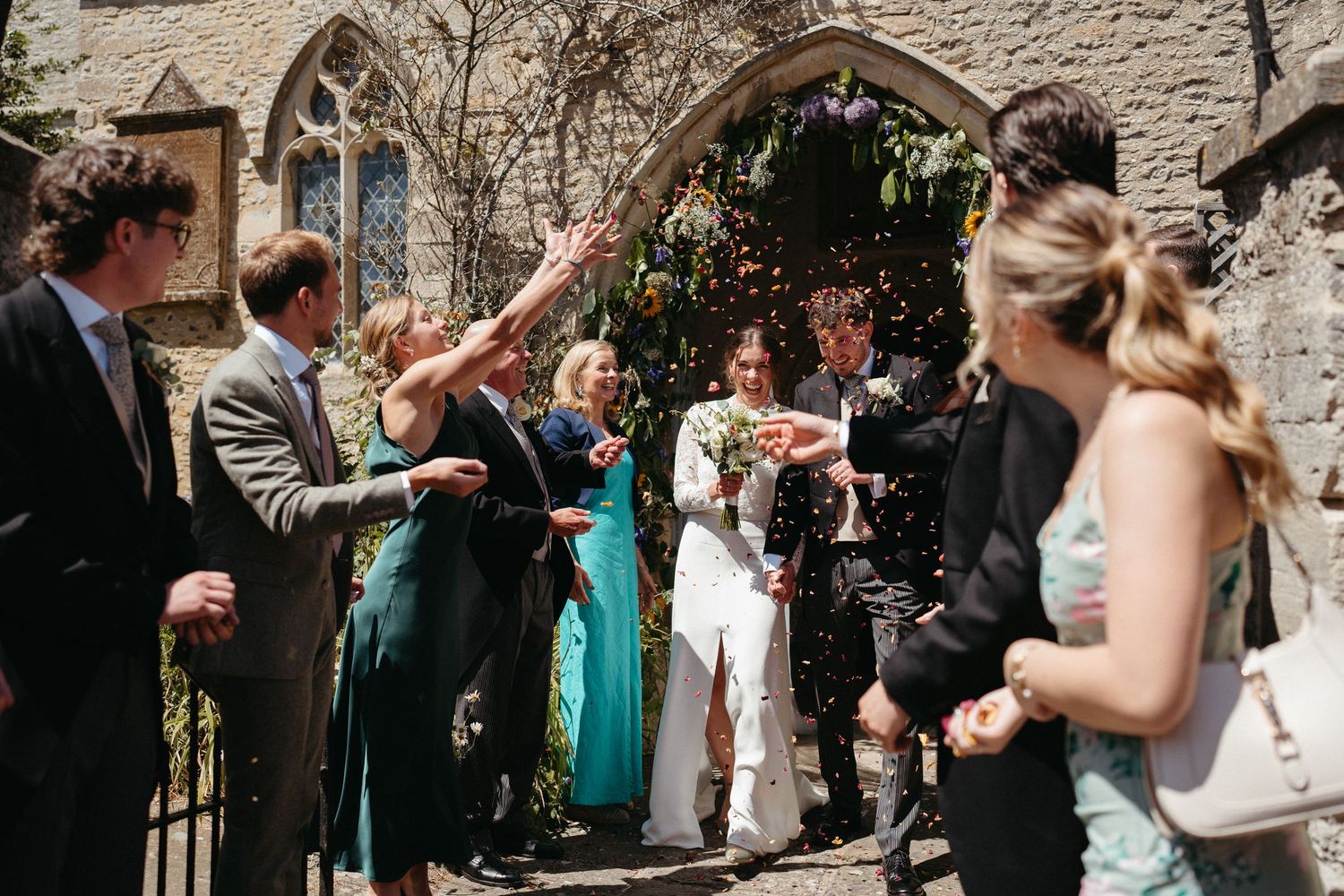 Wedding guests gather outside stone church walls during summer celebration.