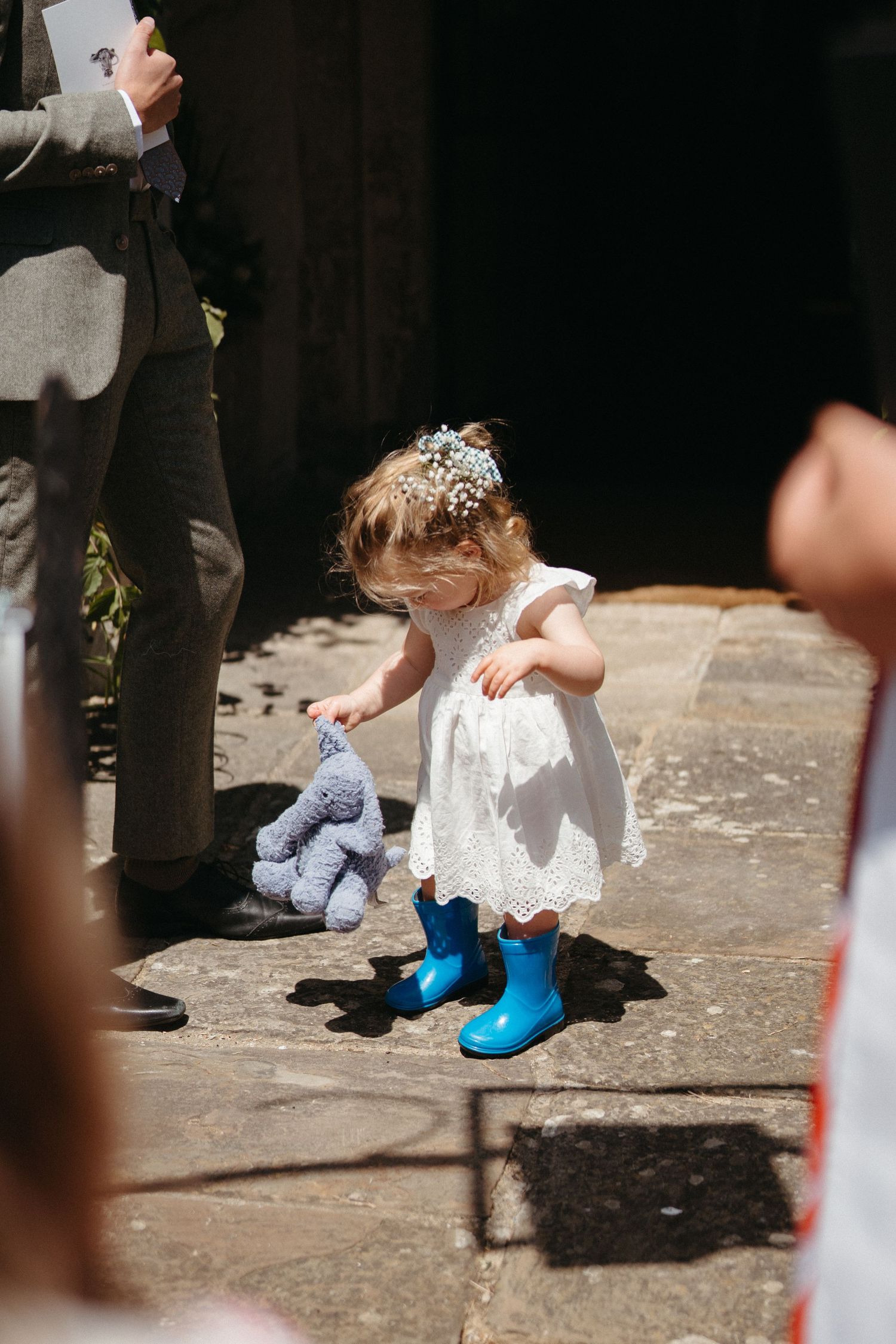 Close-up view of white lace dress and bright blue shoes on stone pavement.