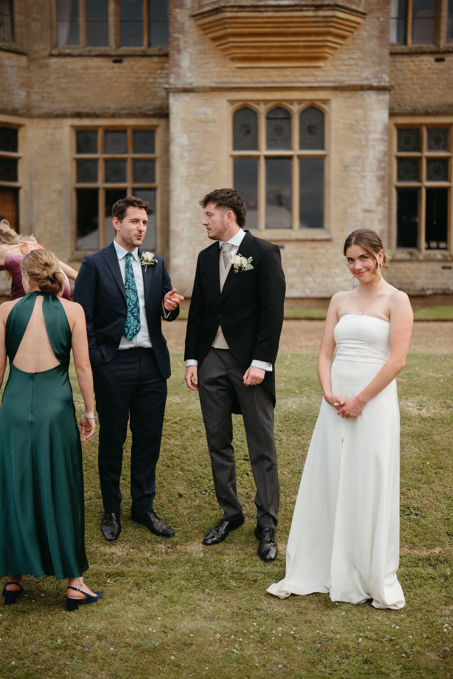 Wedding party poses creatively on the lawn of a historic stone mansion in formal attire.