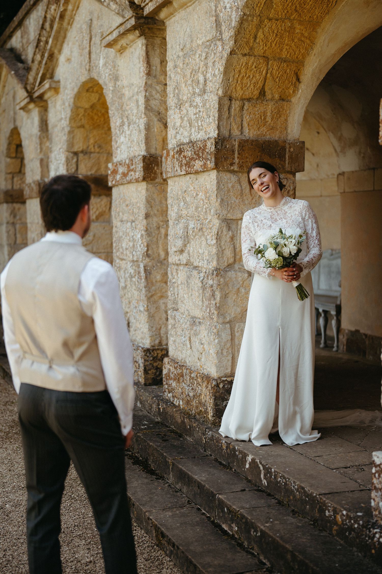 A couple shares a romantic moment under historic stone arches with sunlight filtering through.