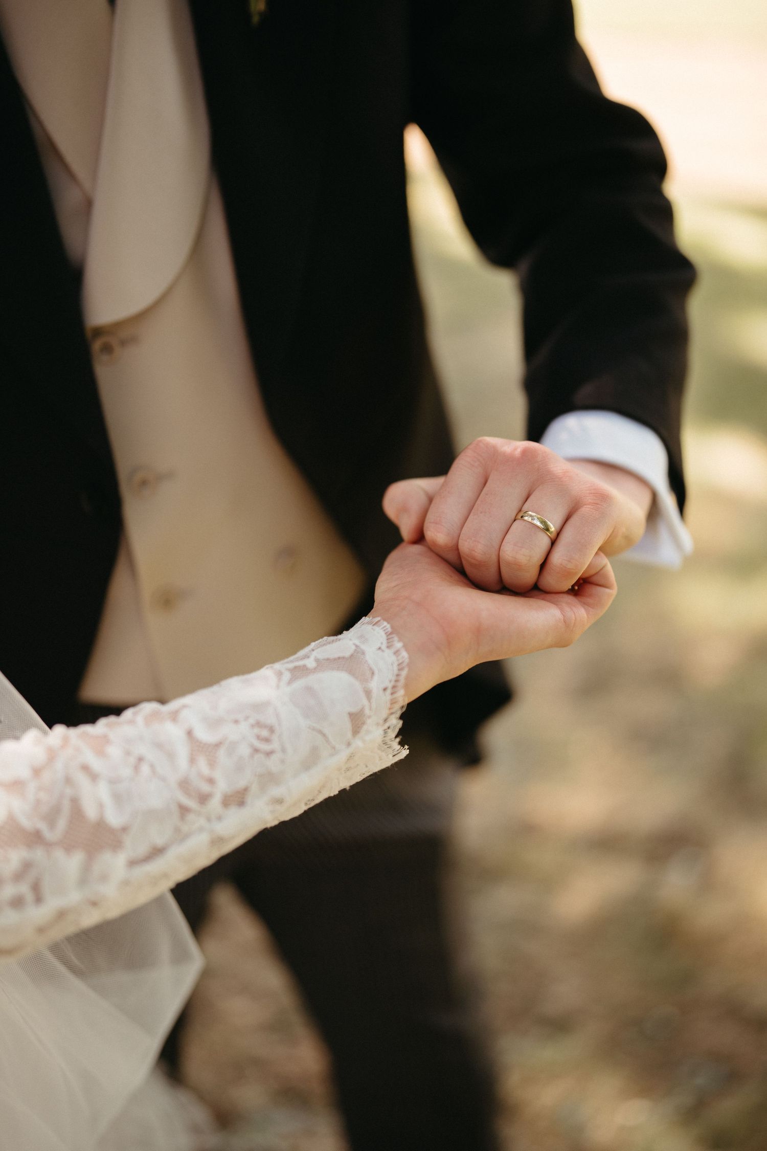 Close-up of clasped hands showing a wedding ring with lace sleeve detail.