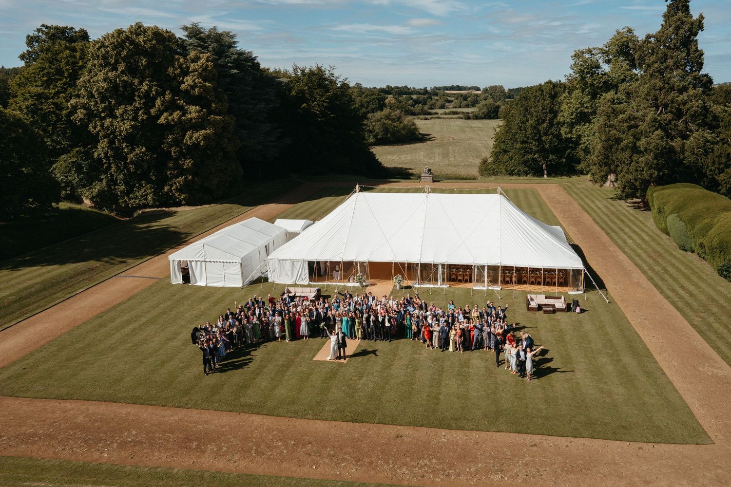 Aerial view of a large white wedding marquee with guests gathered on a manicured lawn.