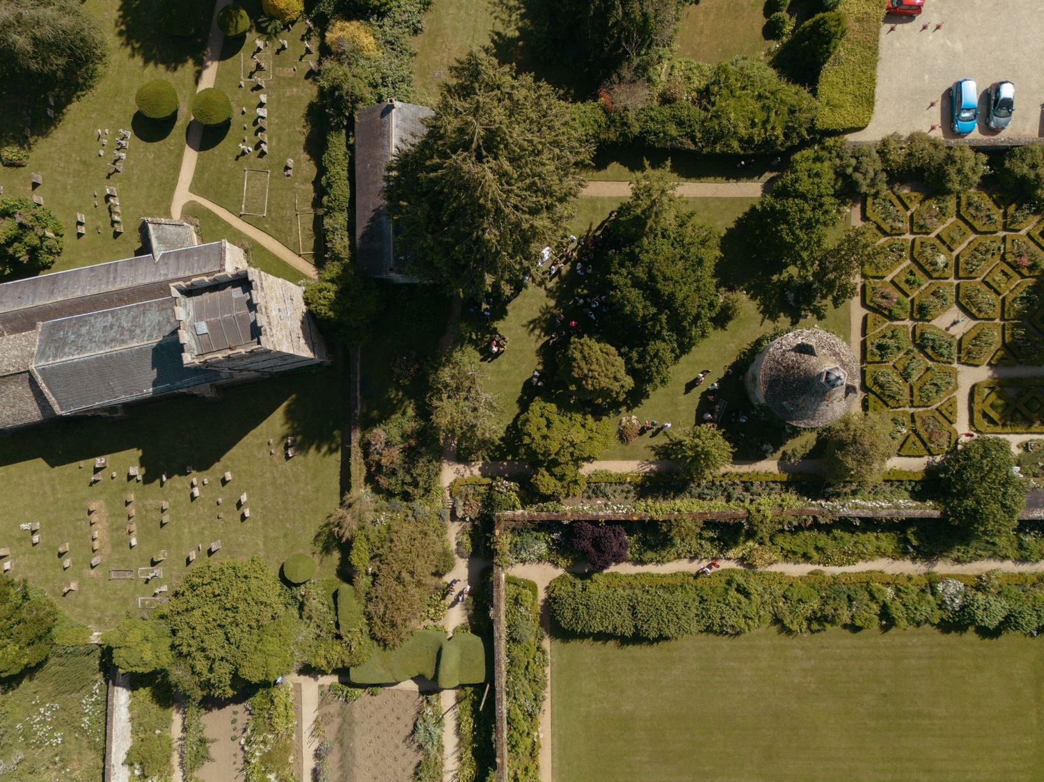 Bird's eye view of an elegant manor house with landscaped gardens and mature trees.