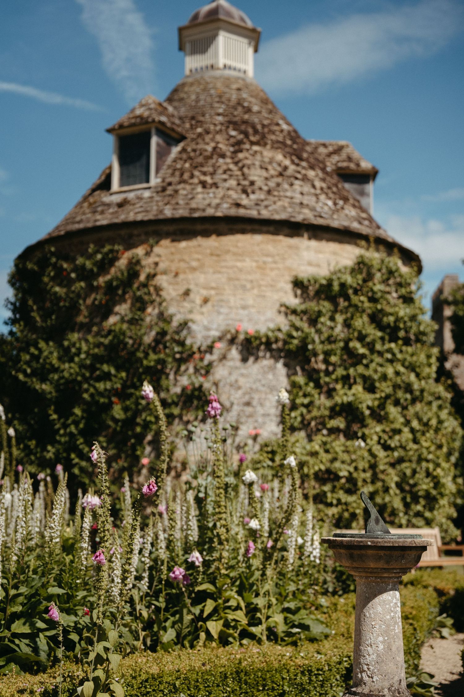 Stone building with ornate architecture surrounded by cottage garden flowers and planters.
