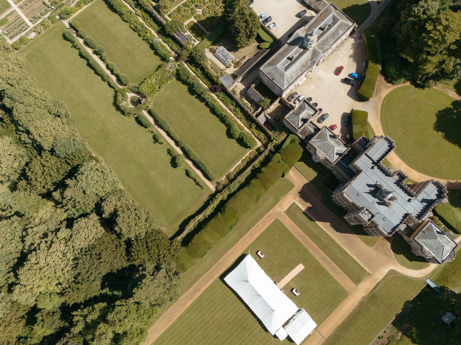 Drone shot of a grand country house with formal gardens and tree-lined grounds.