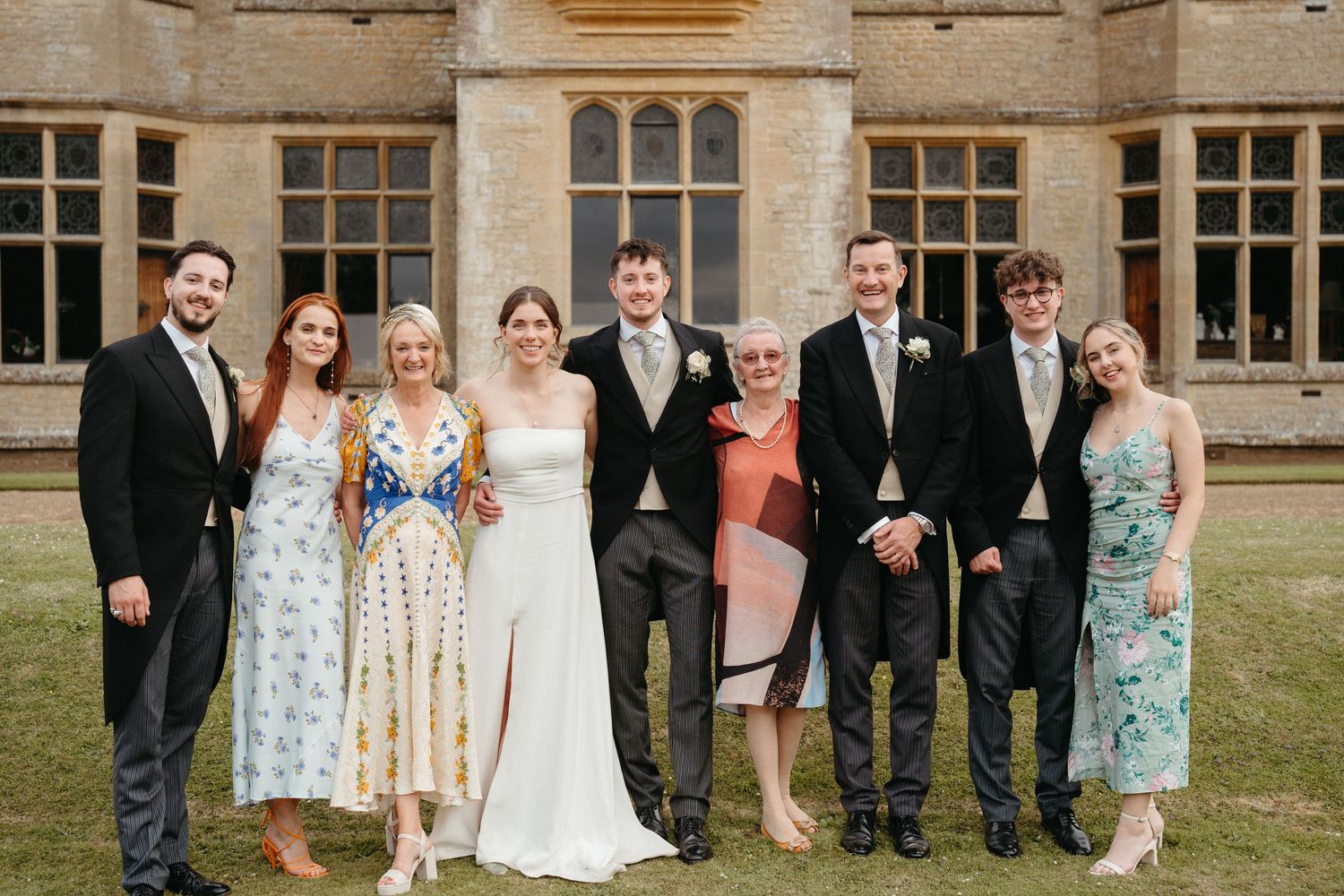 Wedding party group portrait in formal attire outside a historic stone building.