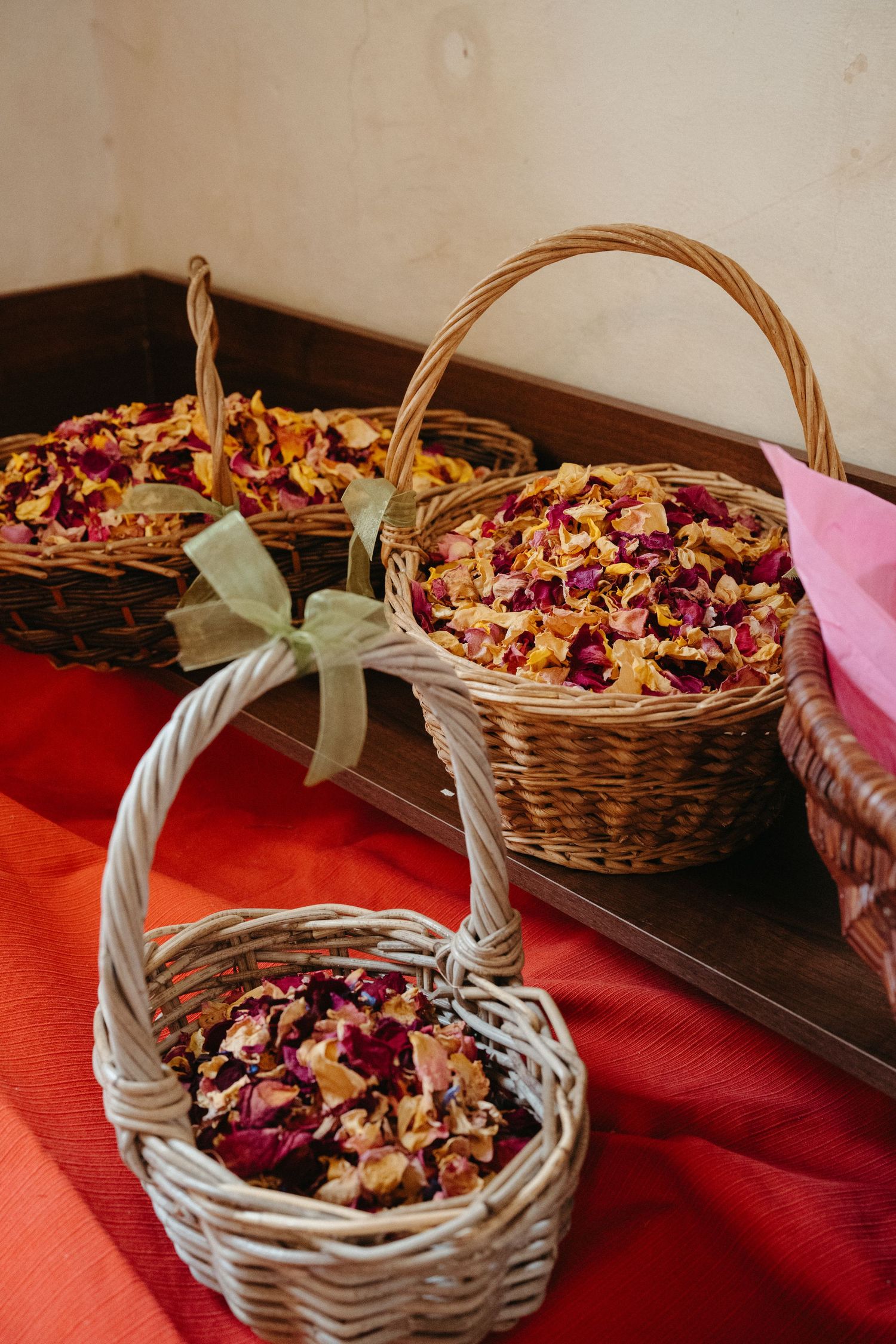 Decorative wicker baskets filled with colorful dried flower petals displayed on red fabric.