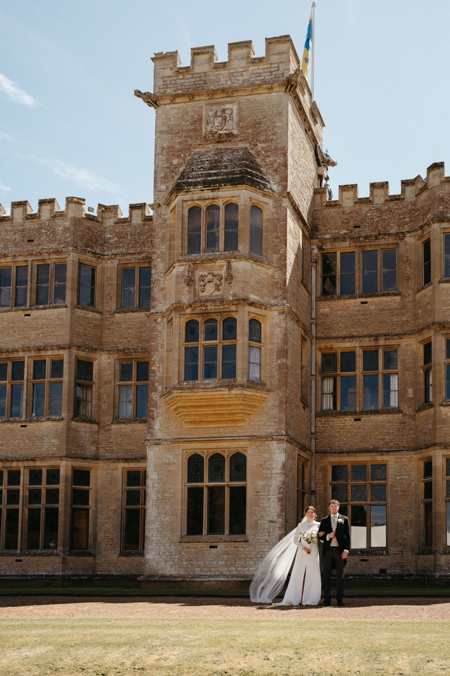 A romantic wedding portrait in front of a majestic stone castle with crenellated towers.