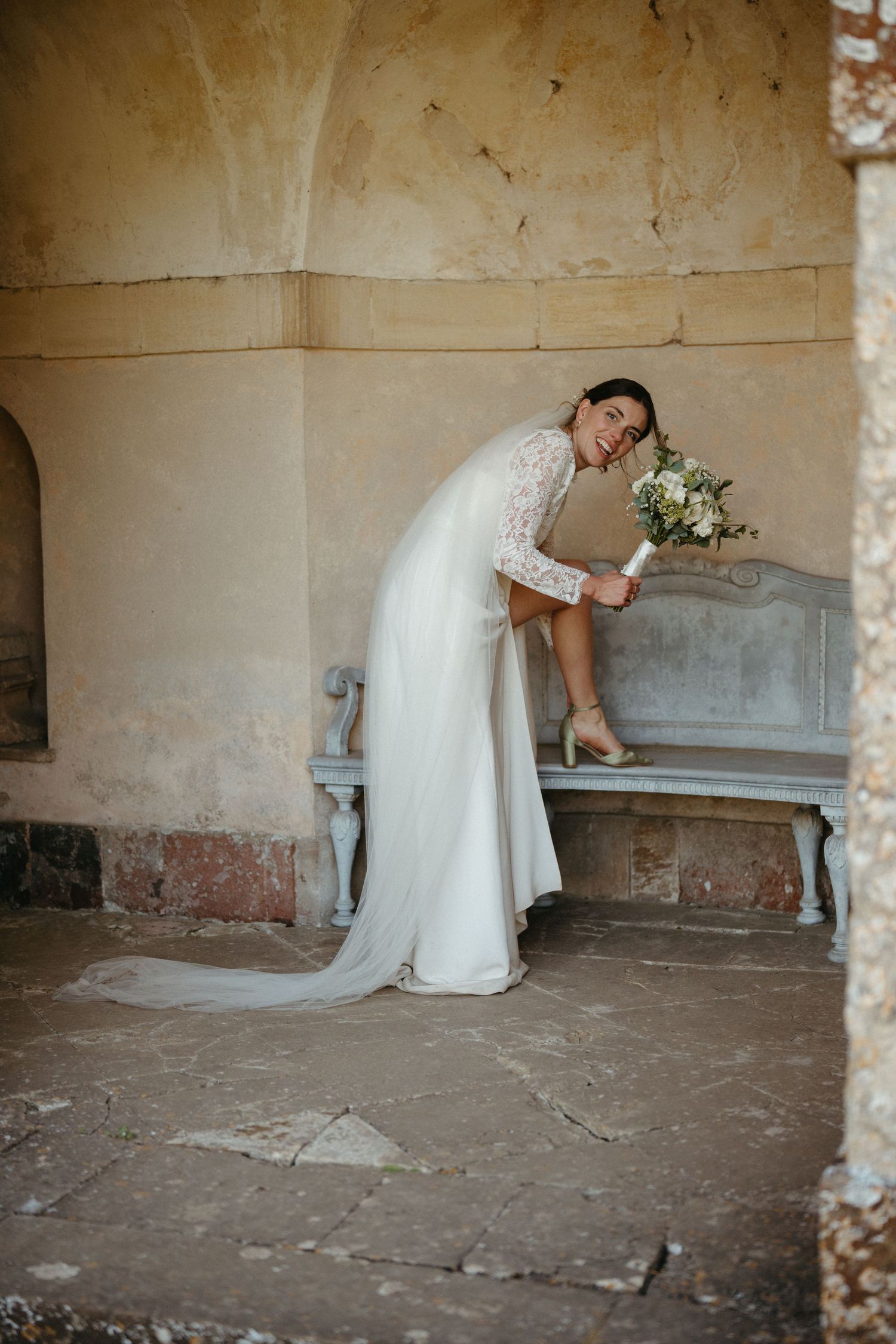 A white bridal gown flows across a stone bench in an atmospheric stone archway.