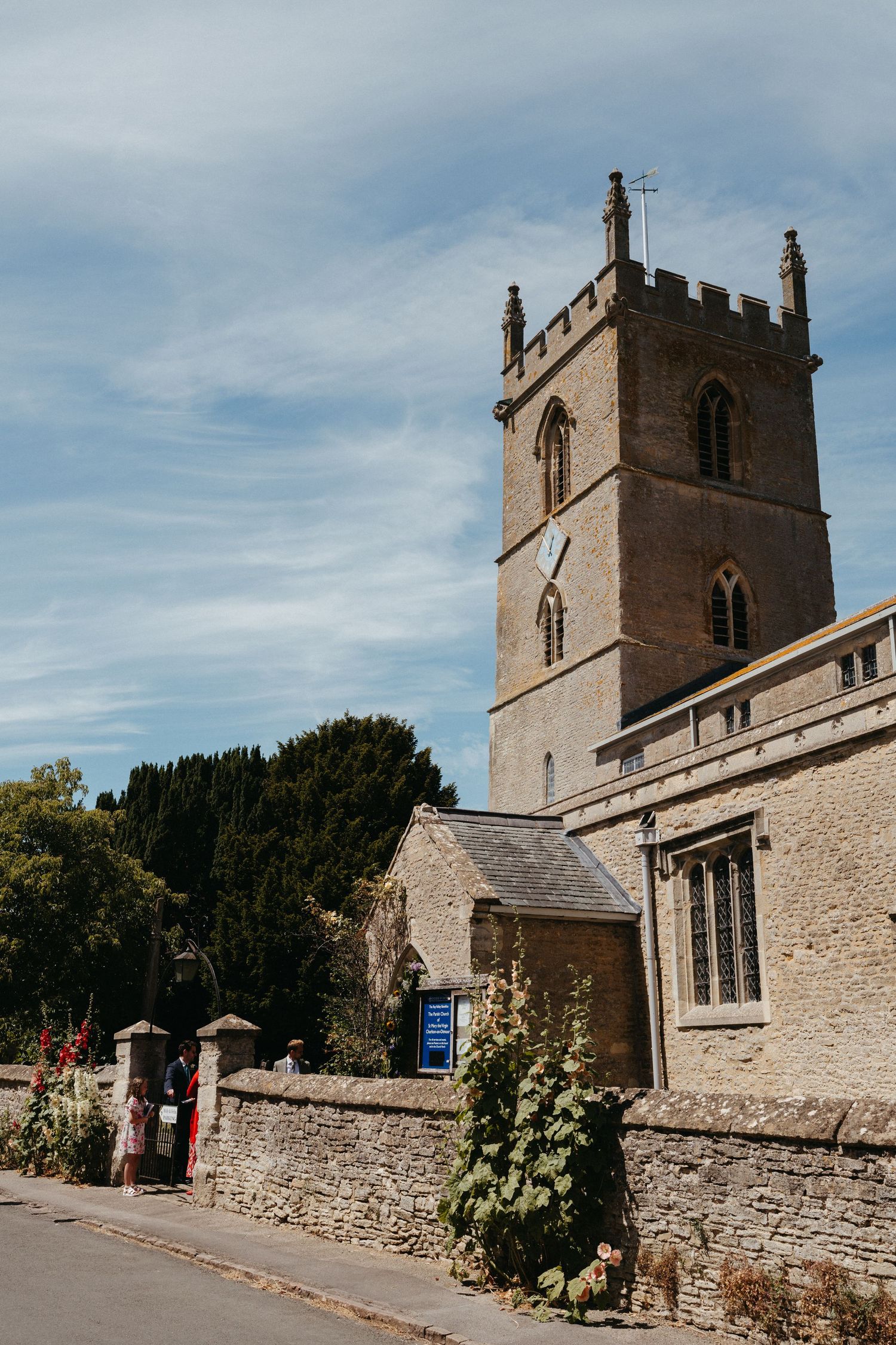 Historic stone church exterior with tall tower and surrounding stone wall on a sunny day.