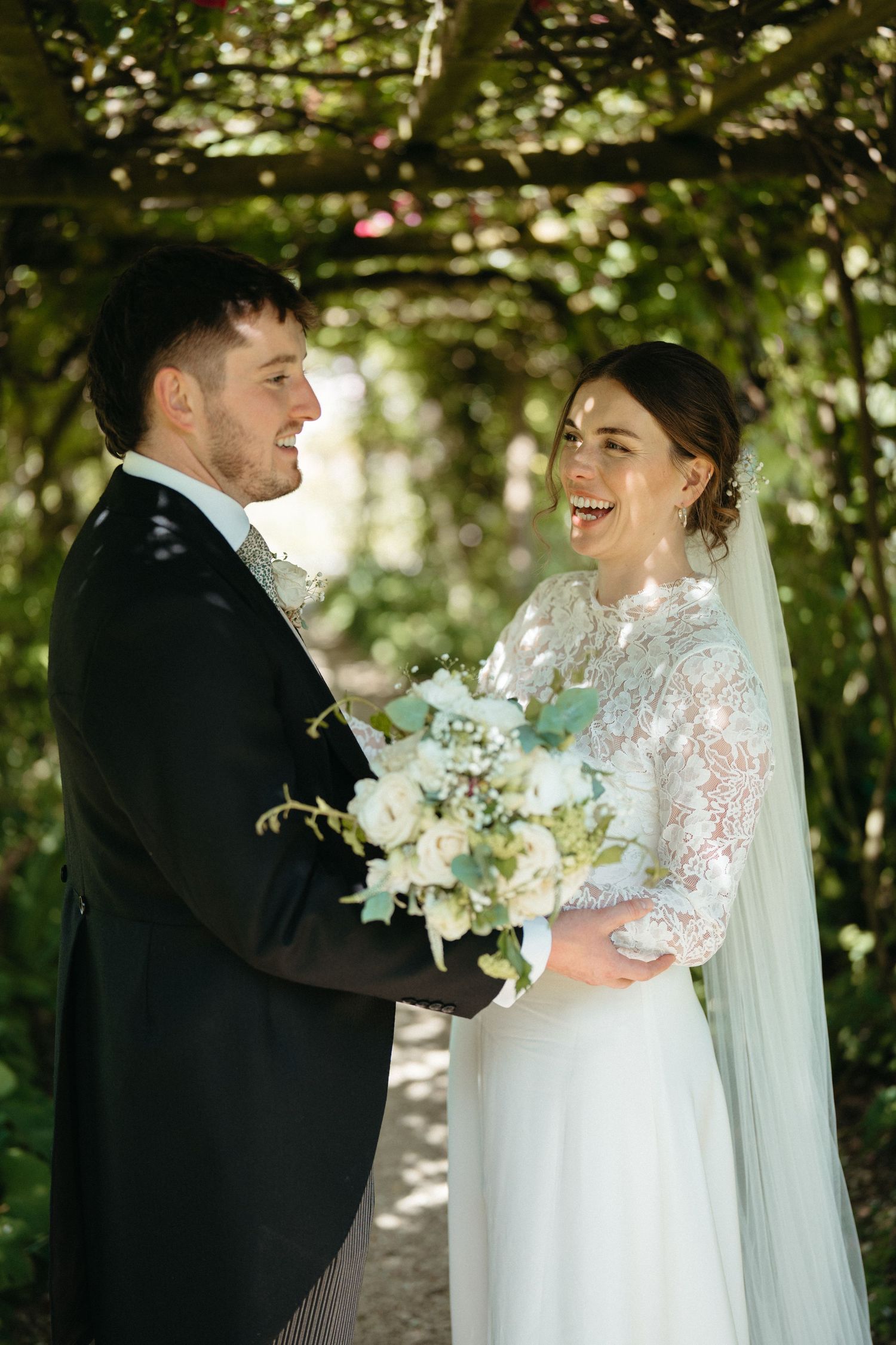 A joyful wedding moment captured between newlyweds under a garden pergola with natural lighting.