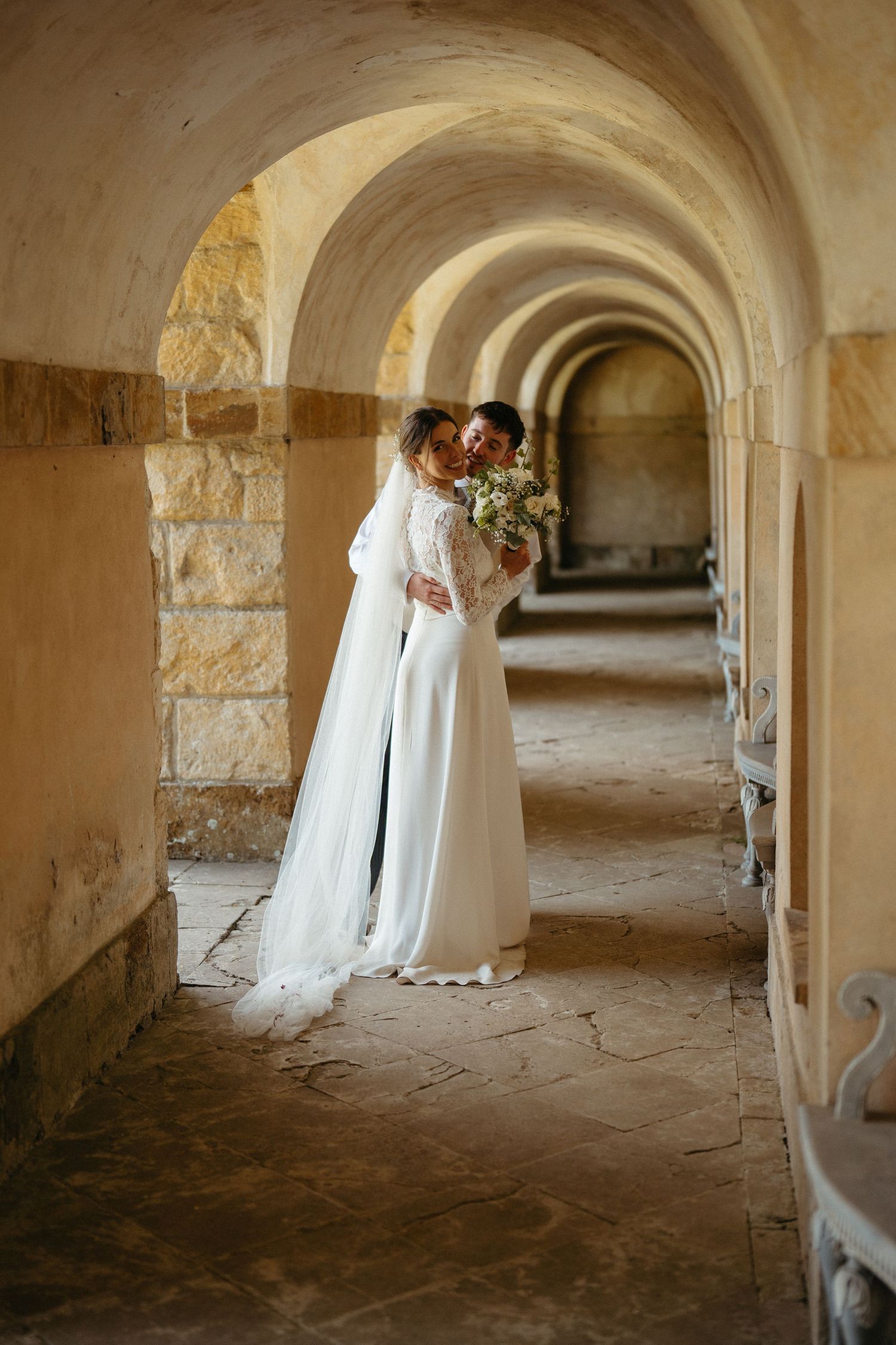 A wedding photoshoot in a dramatic stone archway corridor with natural lighting.