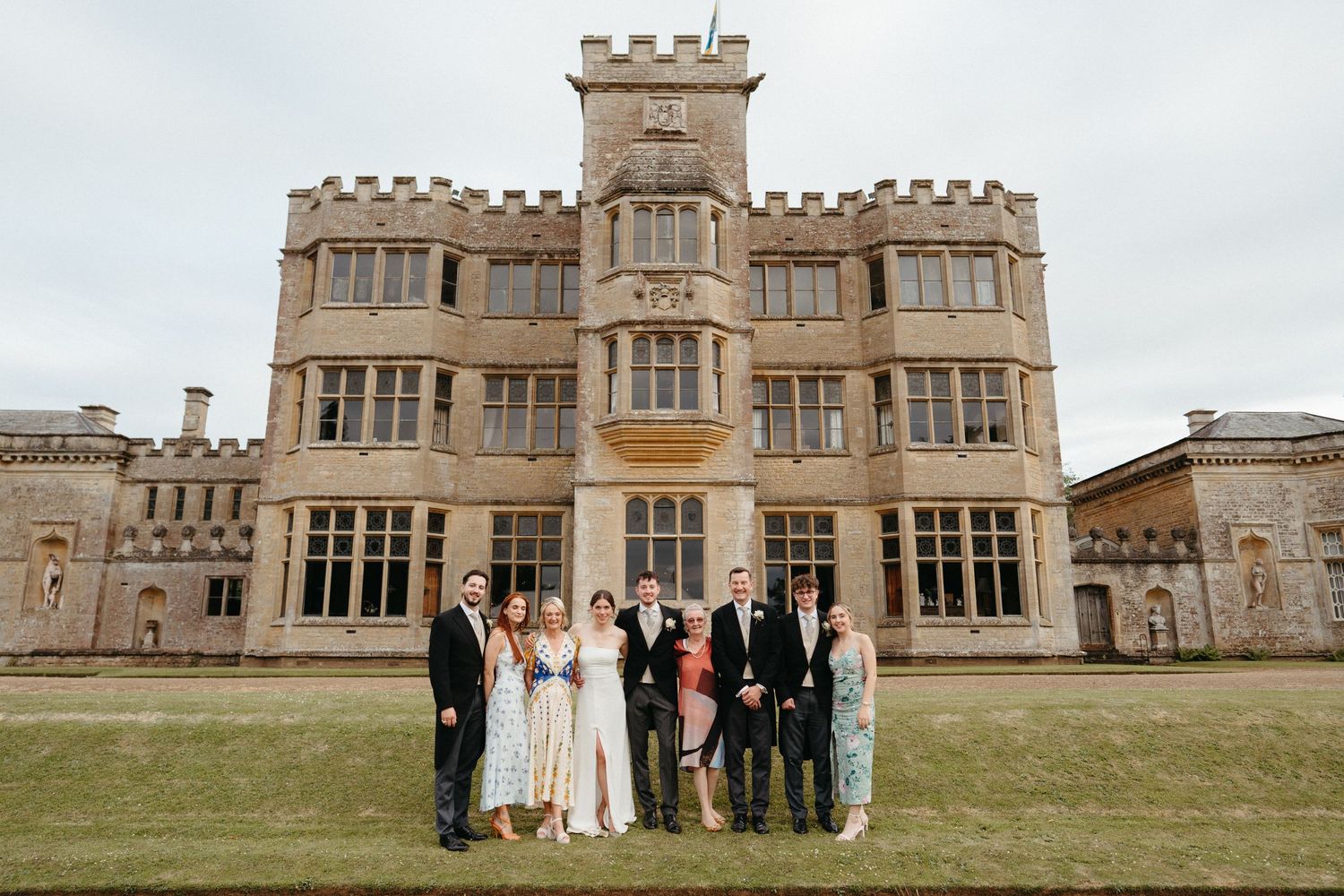 Group photo of wedding party in front of a grand castle-style manor house.
