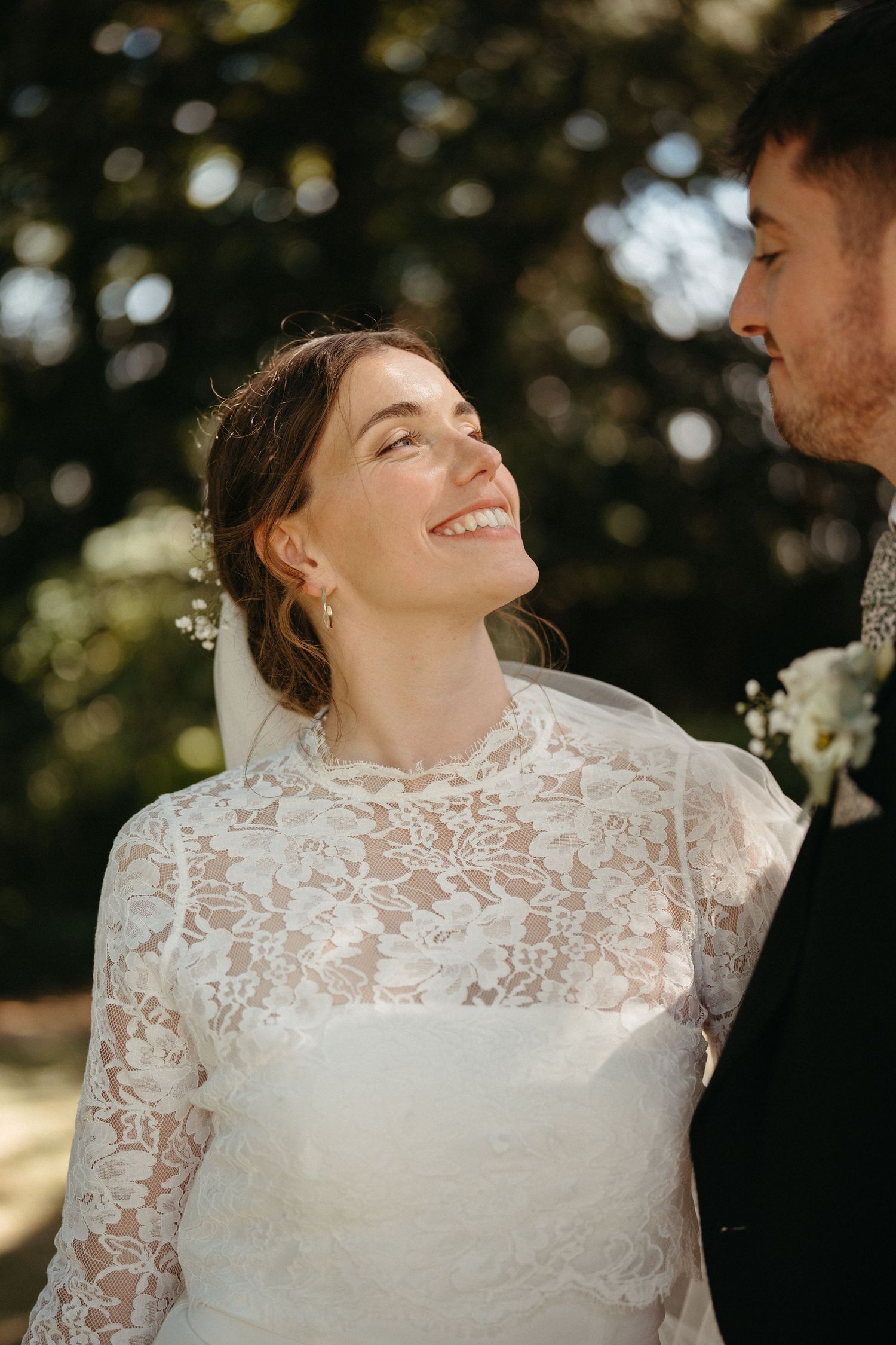 An intimate wedding portrait showing a close moment between newlyweds under sunlit trees.