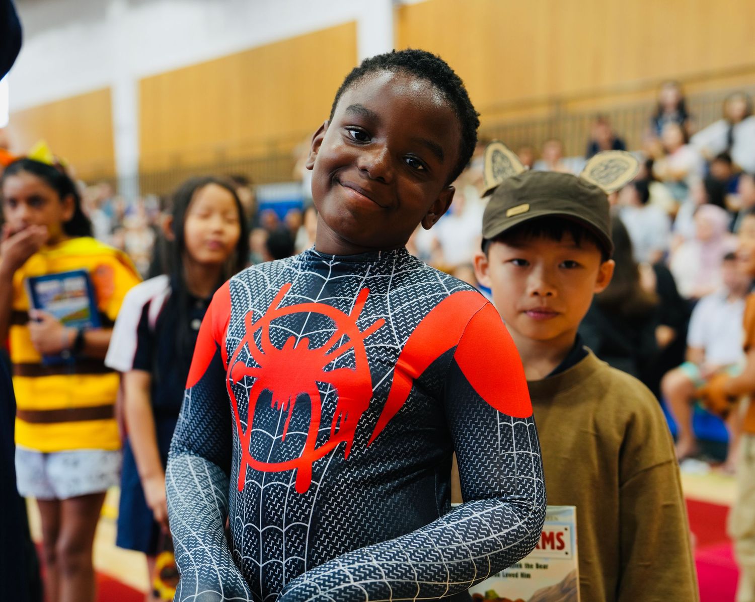 Students in superhero costumes gather during a school event in a gymnasium.
