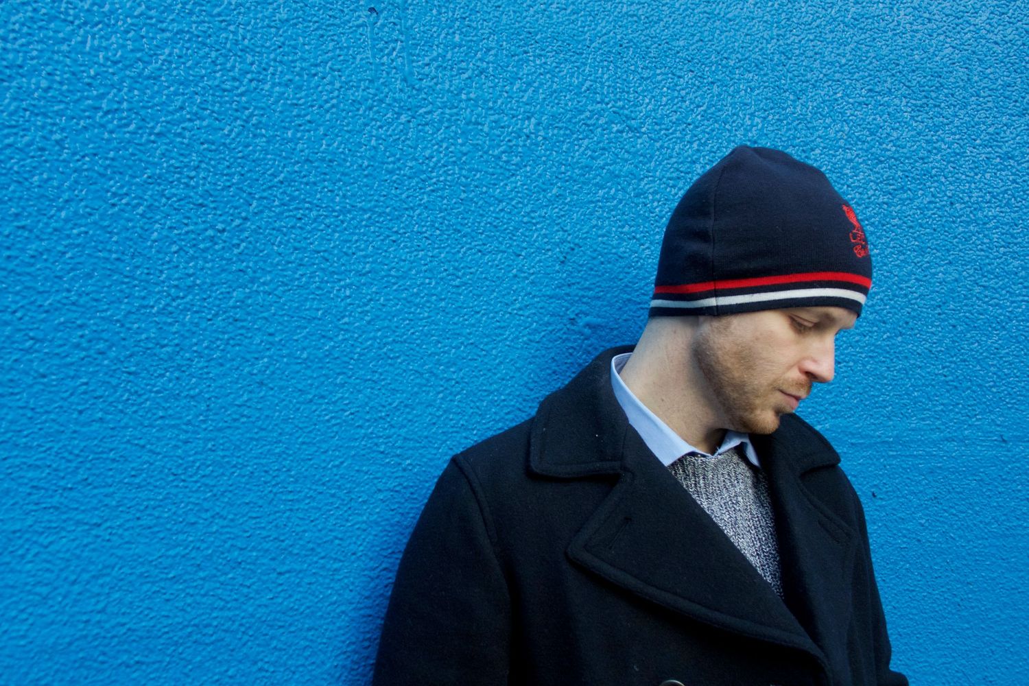 Person in winter coat and beanie against vibrant blue wall looking sideways.