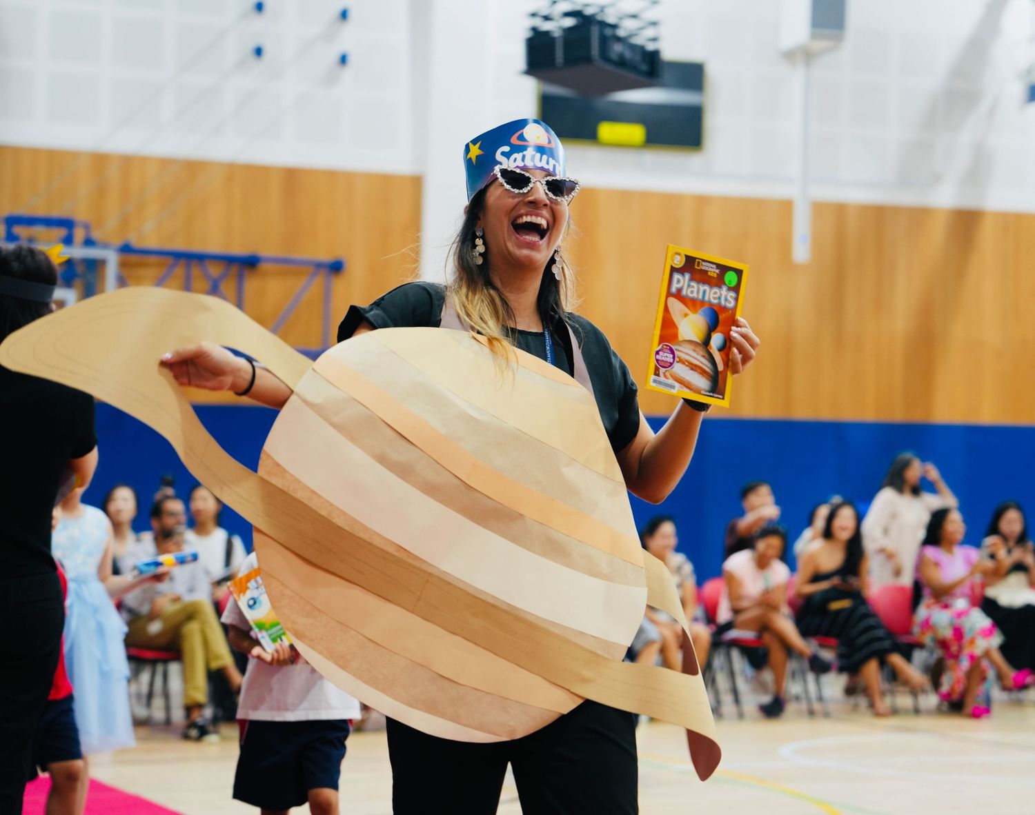 Students holding wooden boards participate in an activity in a school gymnasium.
