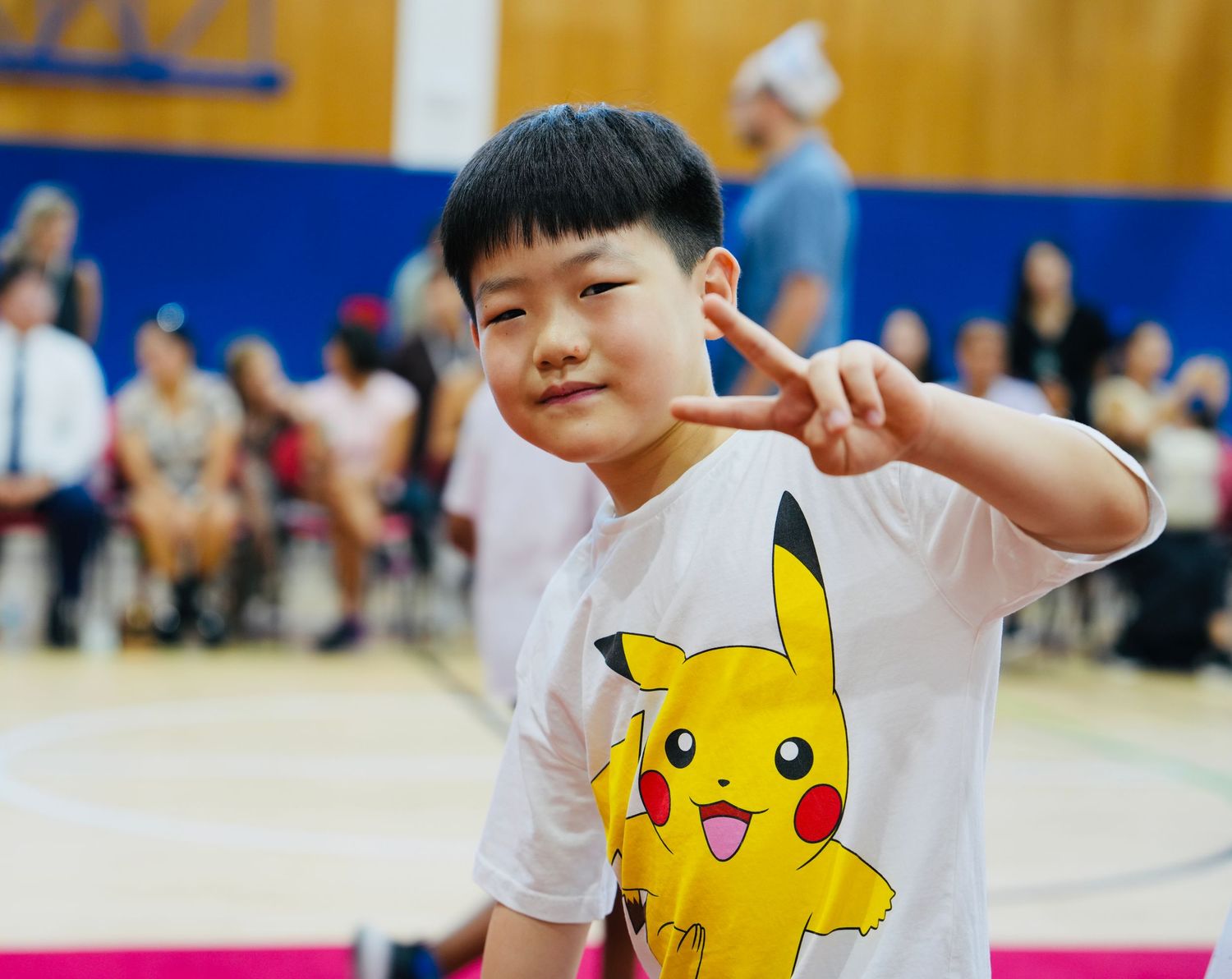 Children holding Pikachu cutouts participate in a school performance on a pink stage.