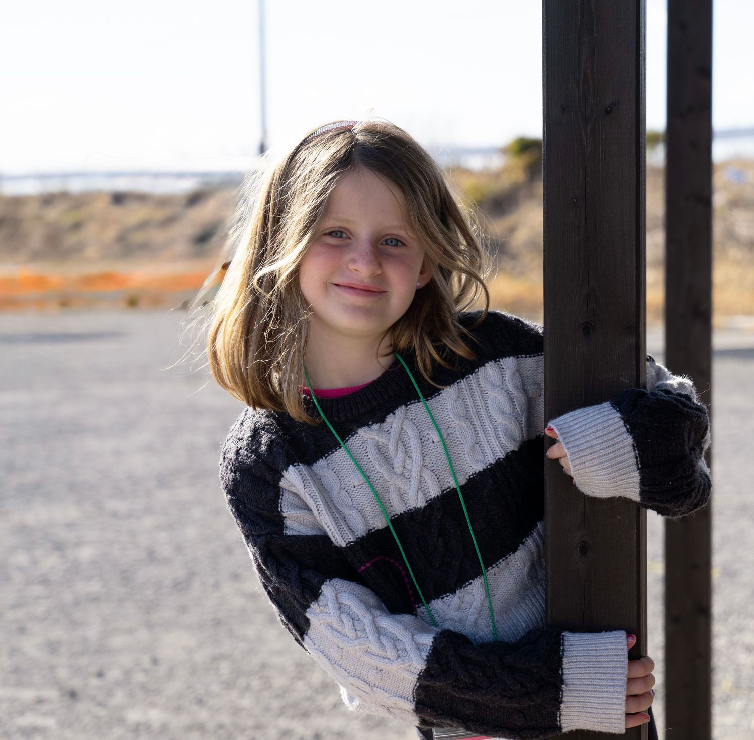 Candid outdoor portrait of someone in a striped sweater leaning against a pole.