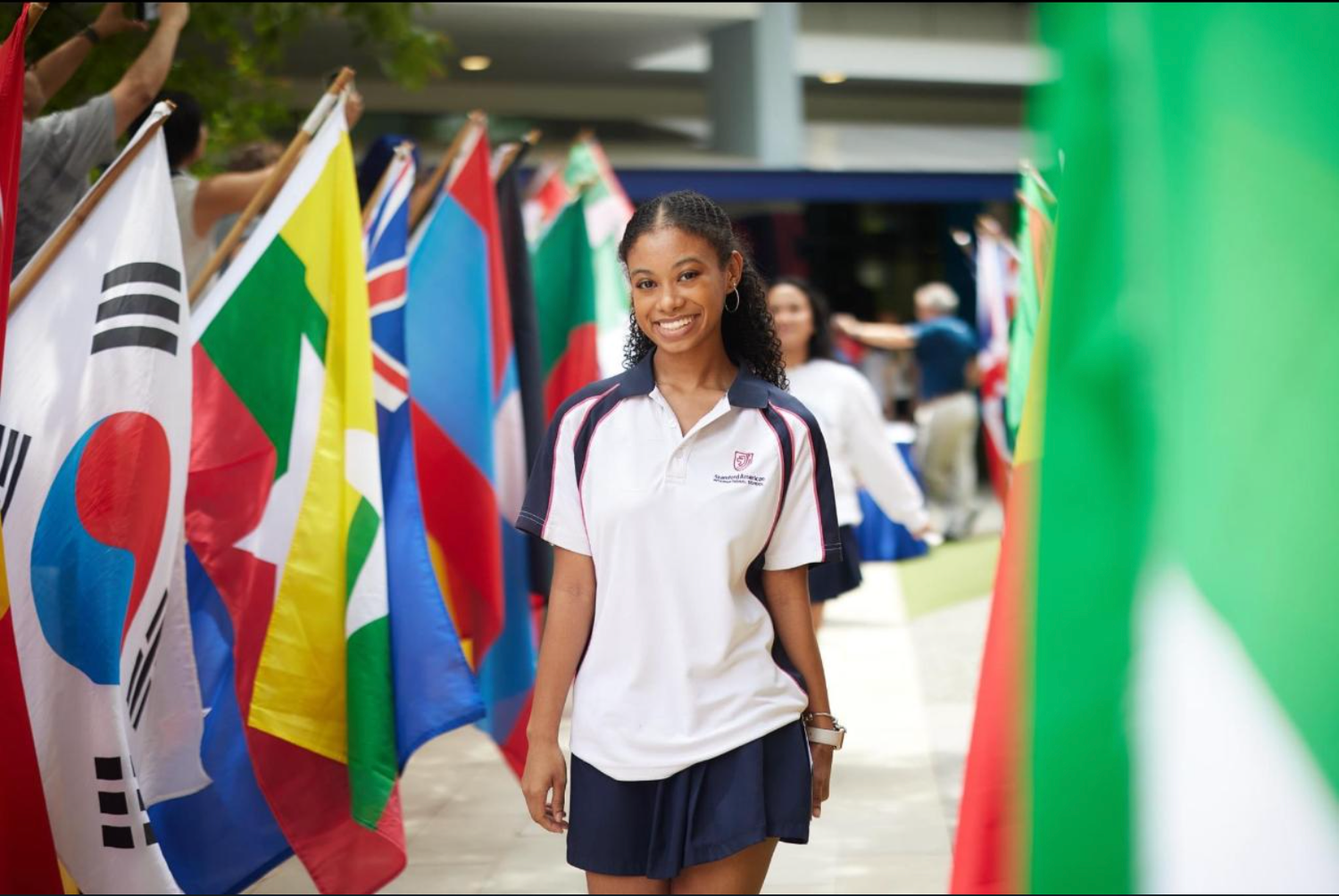 Student in uniform standing in front of international flags display at school event.