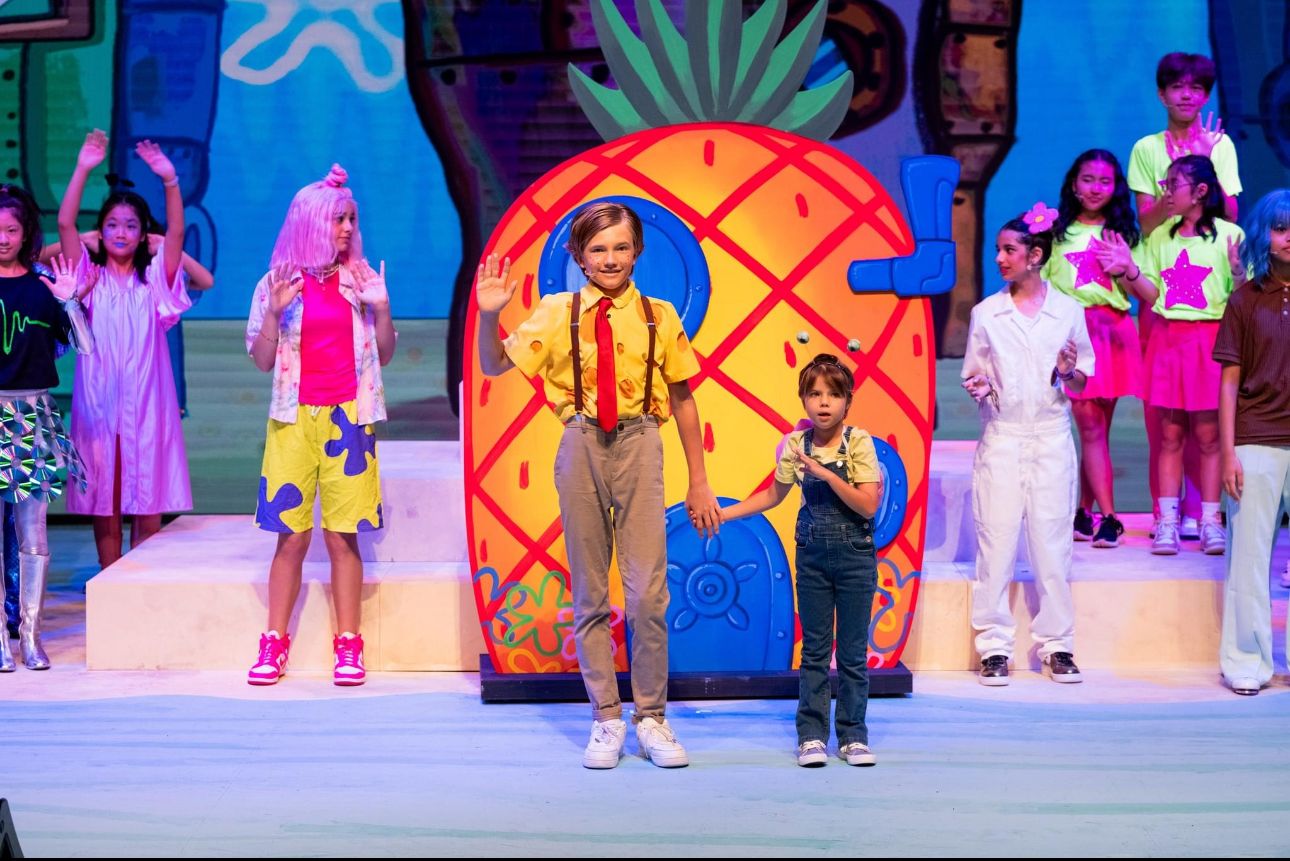 Colorful stage performance with pineapple backdrop and performers in bright costumes.