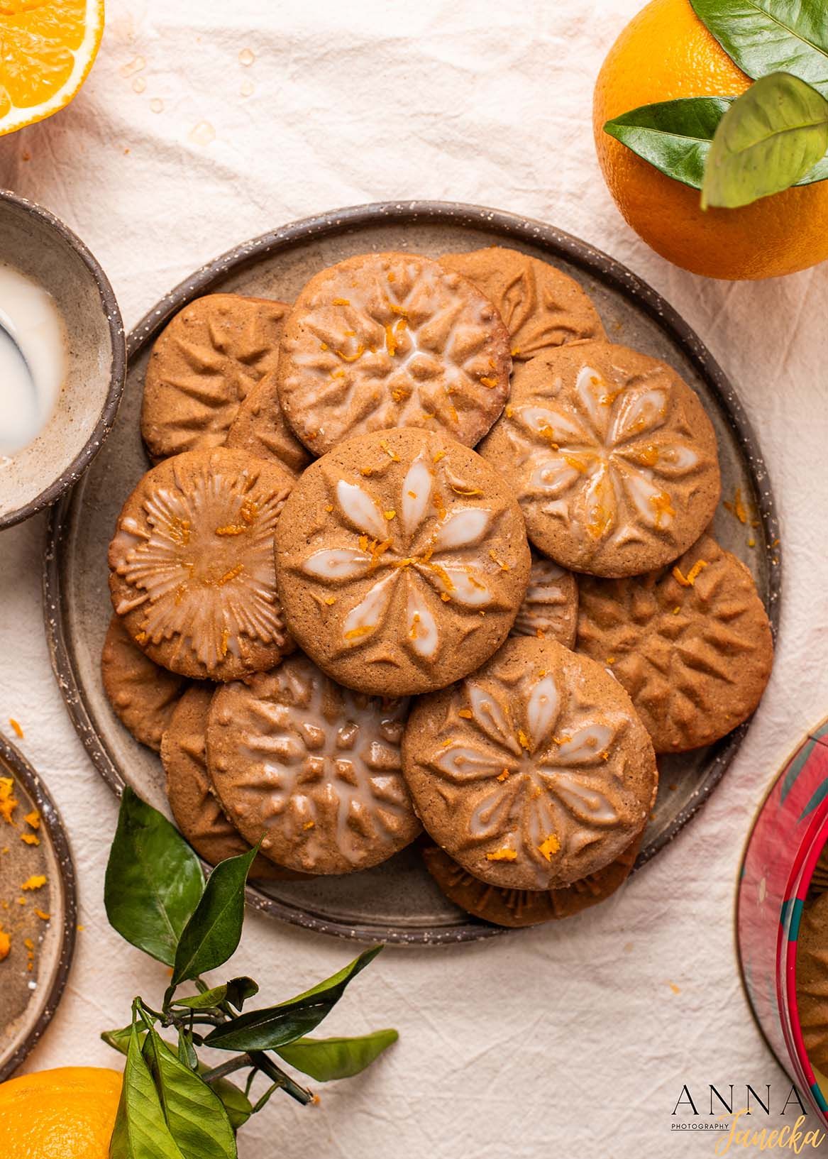 Decorated brown cookies with floral patterns arranged on a rustic plate with orange garnish.