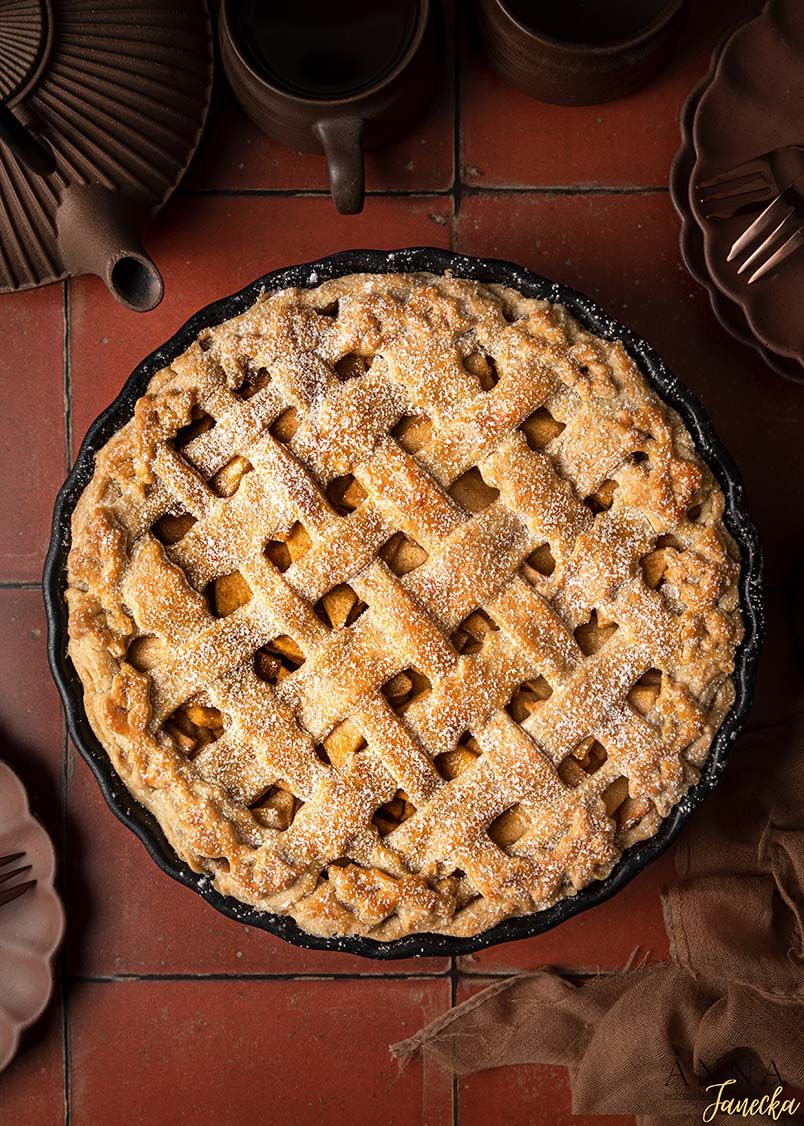 Homemade lattice apple pie dusted with powdered sugar in a dark pie dish.
