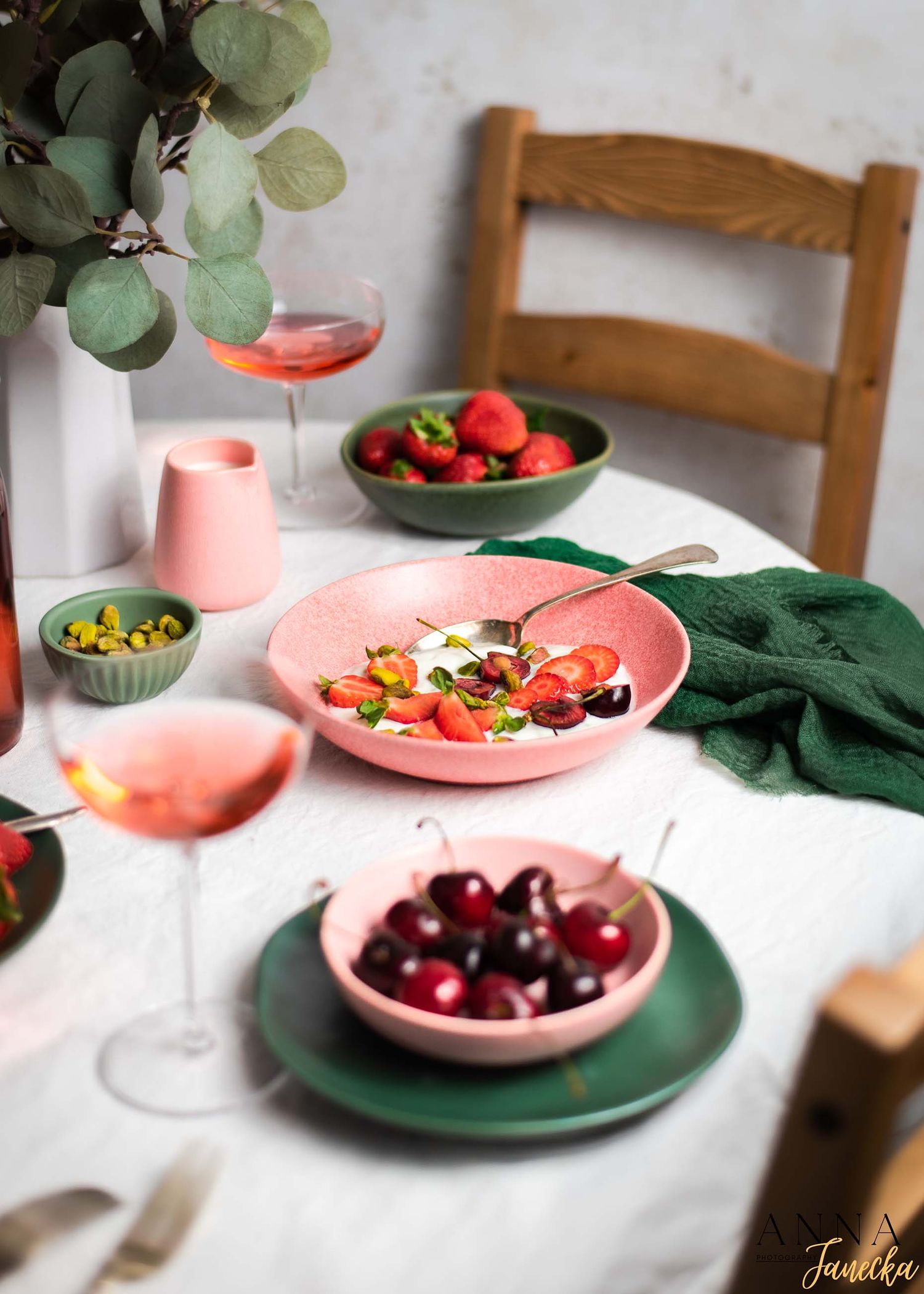 Table setting with pink plates and bowls filled with fresh cherries and strawberries.