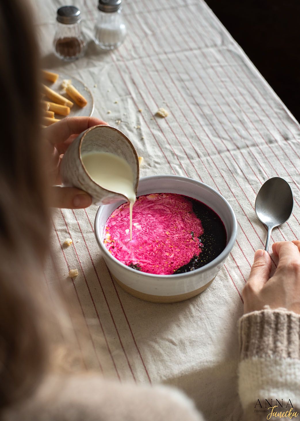 Pouring cream over bright pink soup or dessert in a white bowl.