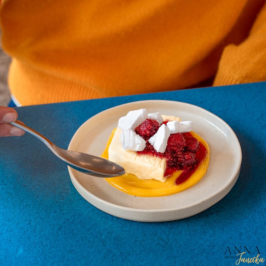 Dessert plate with vanilla cream and raspberry sauce on bright blue table surface.