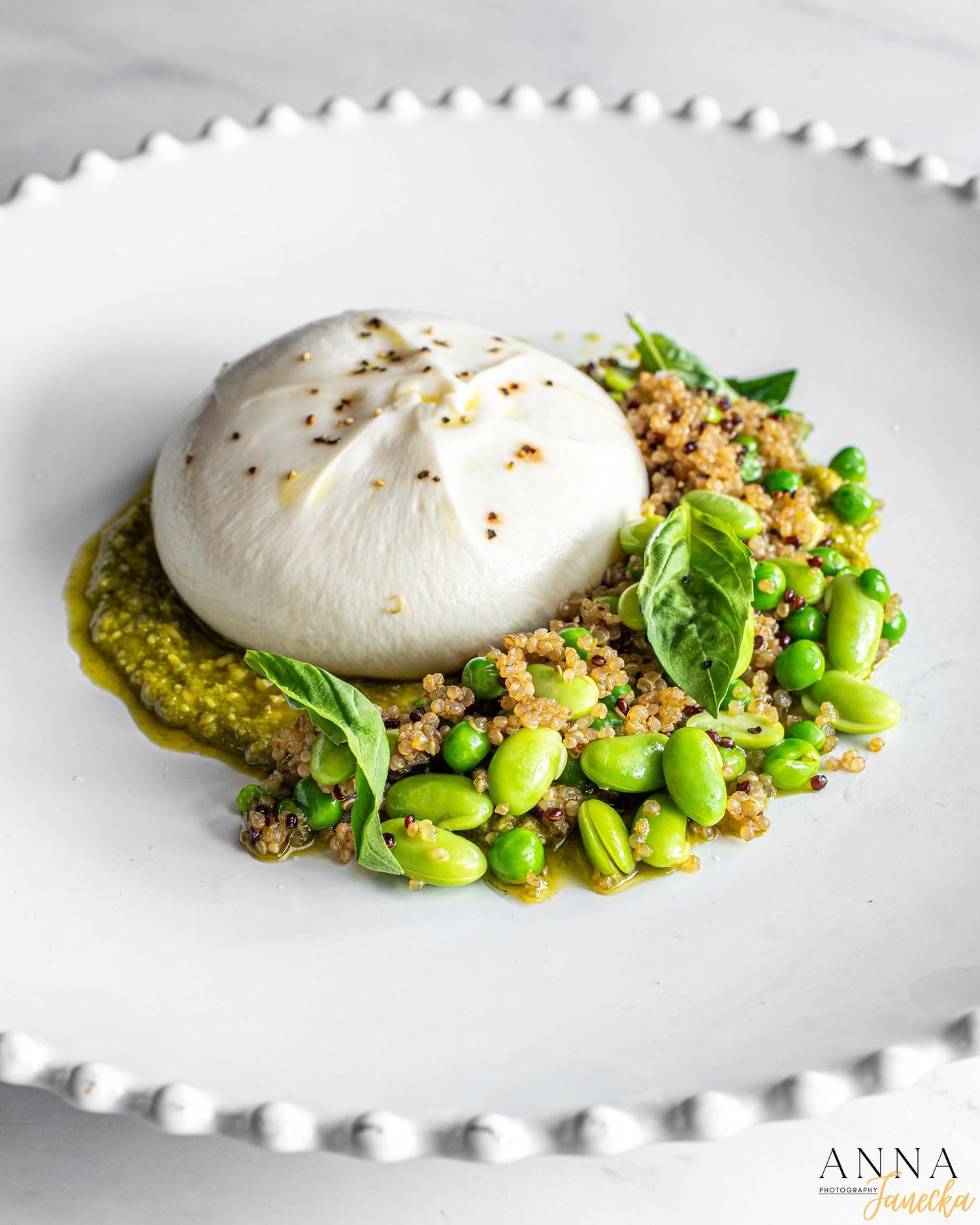Poached egg over green pesto sauce with edamame beans and crispy breadcrumbs on a white plate.