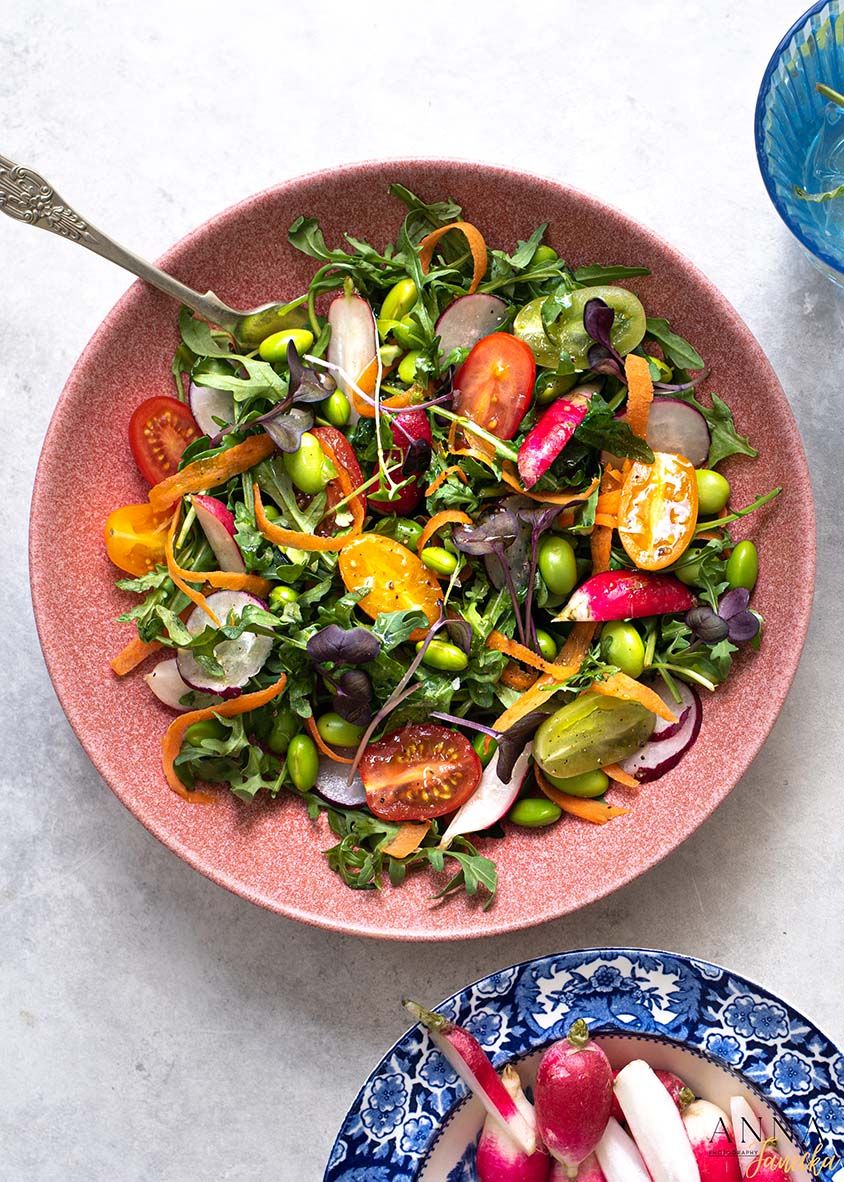 Colorful garden salad with cherry tomatoes, edamame, and mixed vegetables in a pink ceramic bowl.