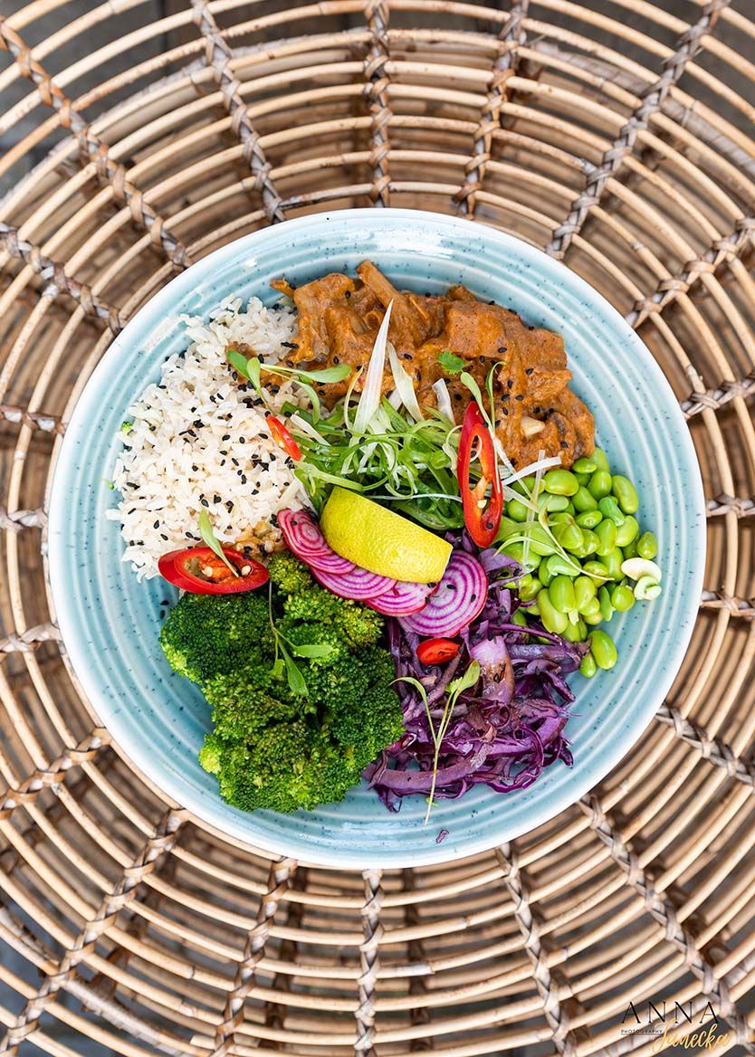 Colorful Buddha bowl with rice, vegetables, and protein on blue plate with bamboo placemat.