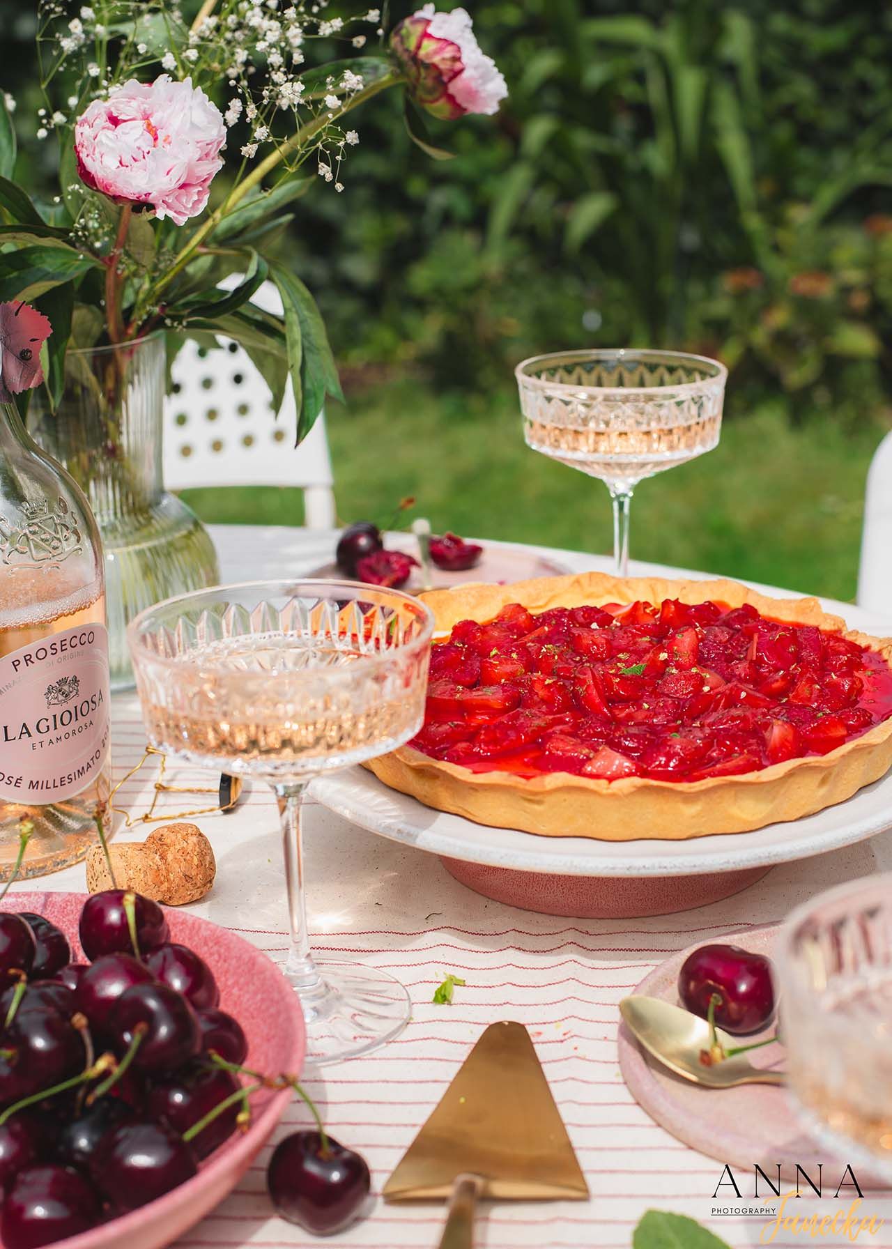 Summer outdoor table setting with fresh cherry tart, champagne glasses and pink flowers.
