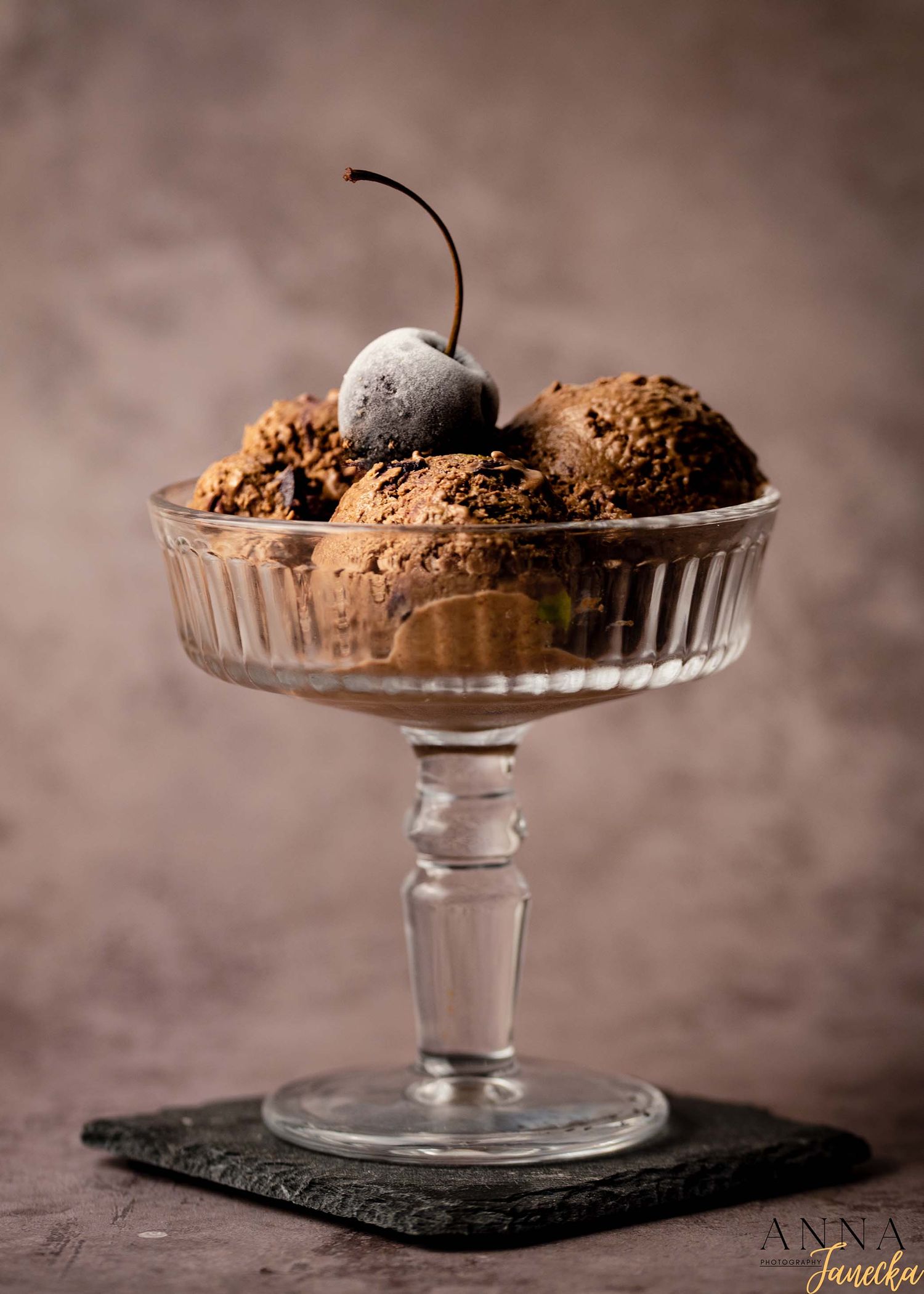 Chocolate dessert with a cherry served on an elegant glass pedestal plate.