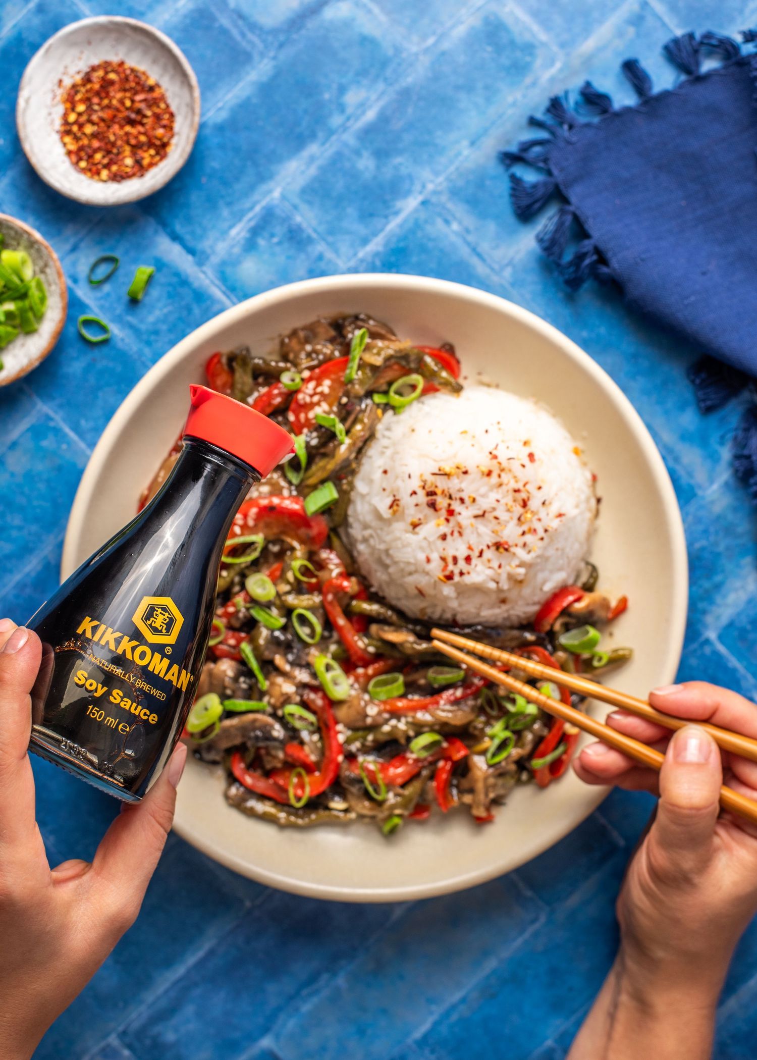 Stir-fried beef and vegetables served with rice and chopsticks on blue tablecloth.