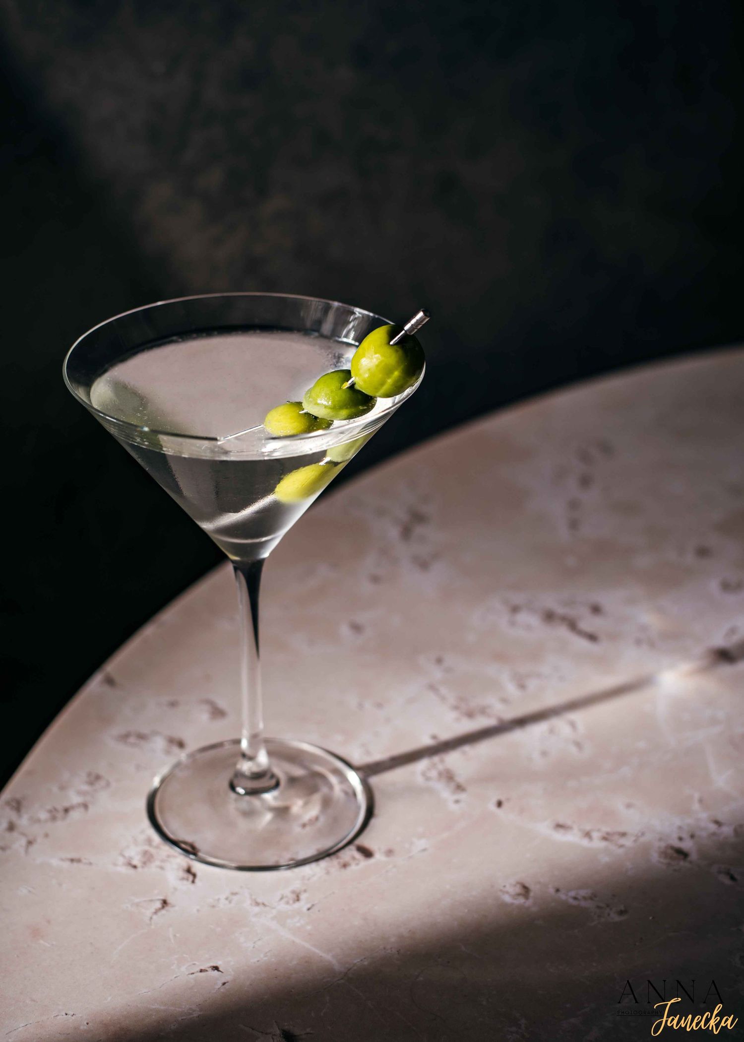 Classic martini cocktail garnished with olives in a stemmed glass on textured surface.
