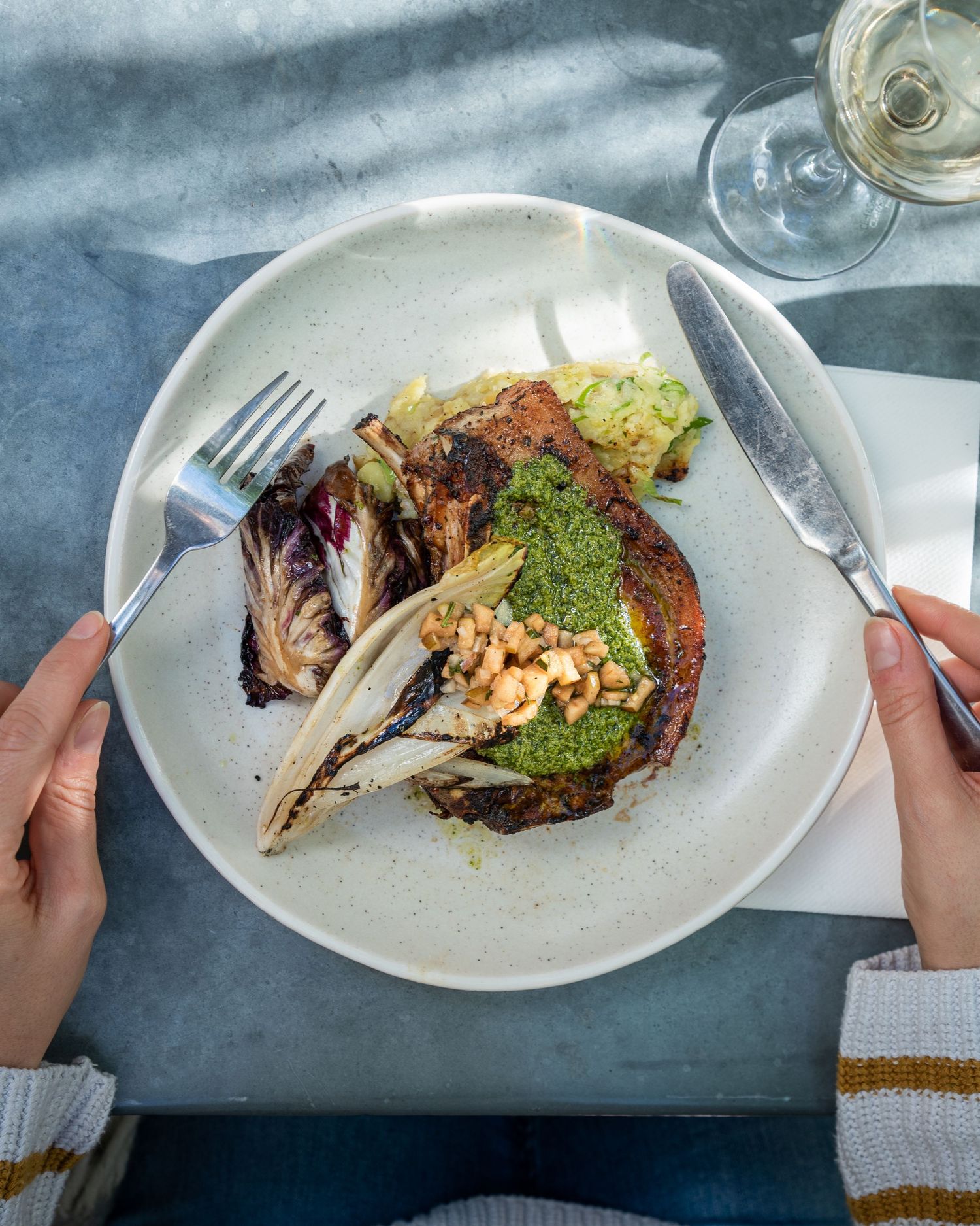 Grilled steak with green sauce and charred vegetables served on a white plate.