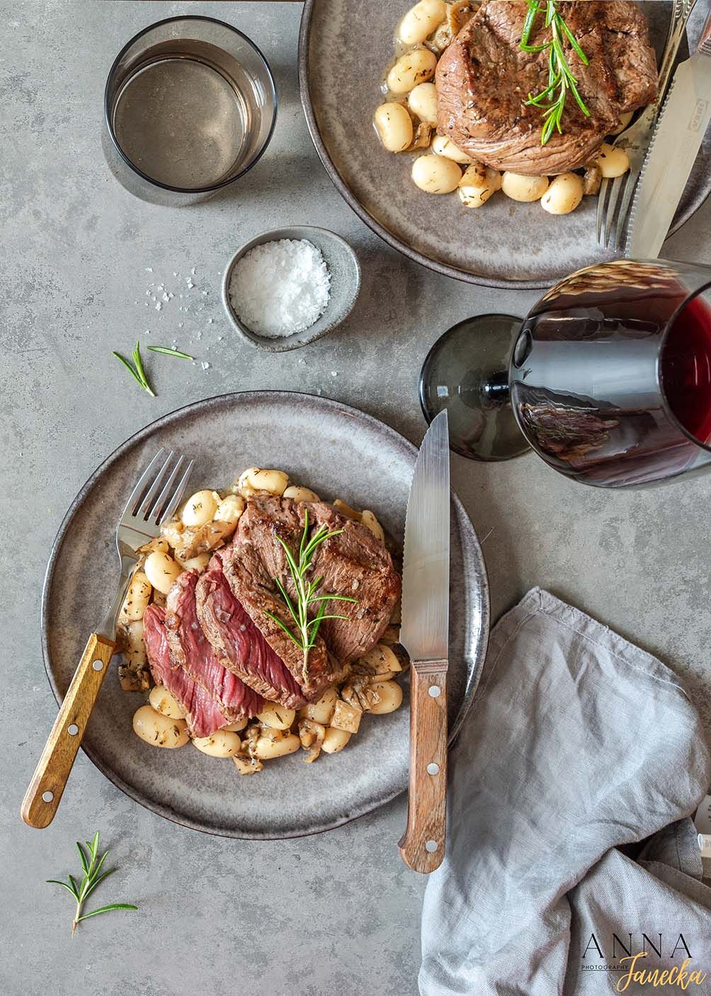 Medium rare steak served with mushrooms on a gray plate with wine glass in background.