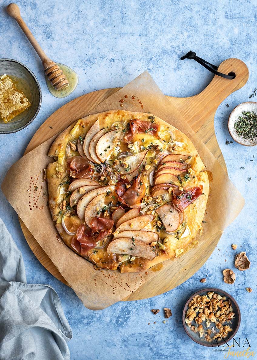 Rustic pizza topped with sliced pears, honey, and herbs on a wooden serving board.