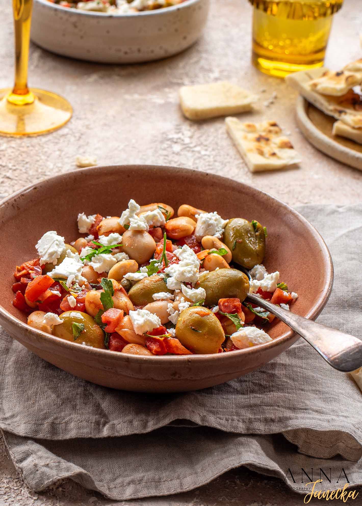 Mediterranean salad with olives, tomatoes, feta cheese and herbs served in a rustic terracotta bowl.
