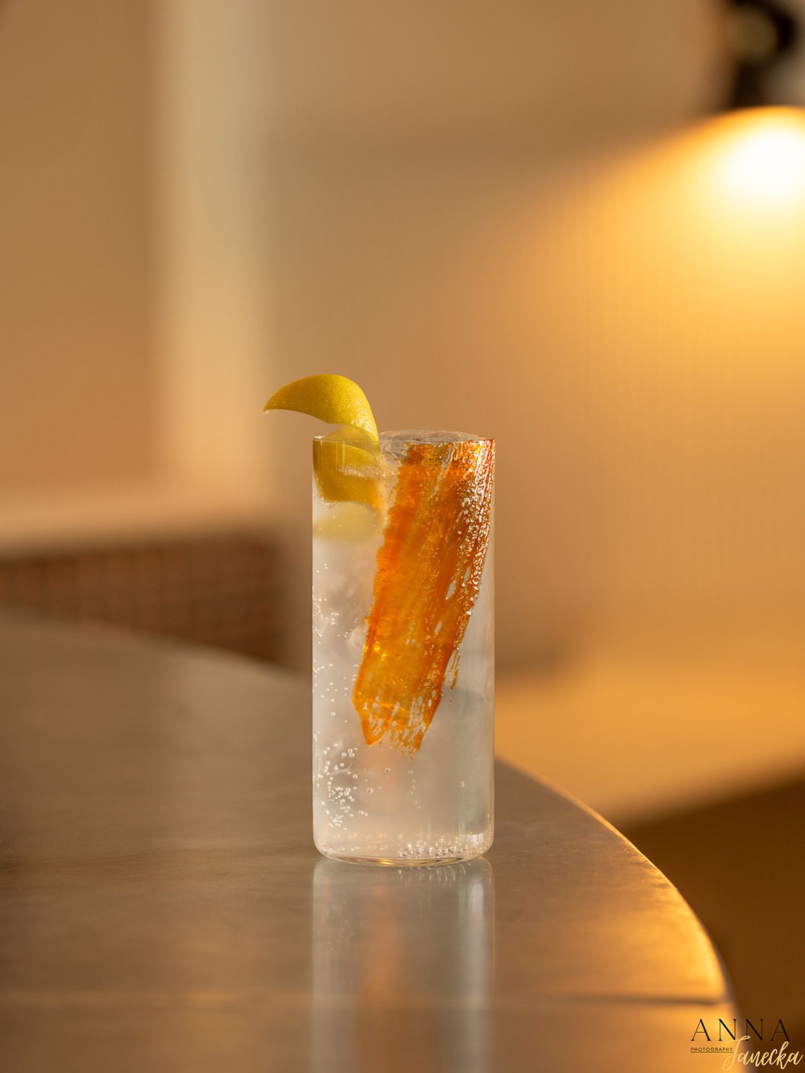 Tall glass of ice-cold cocktail garnished with citrus peel and lemon wedge.