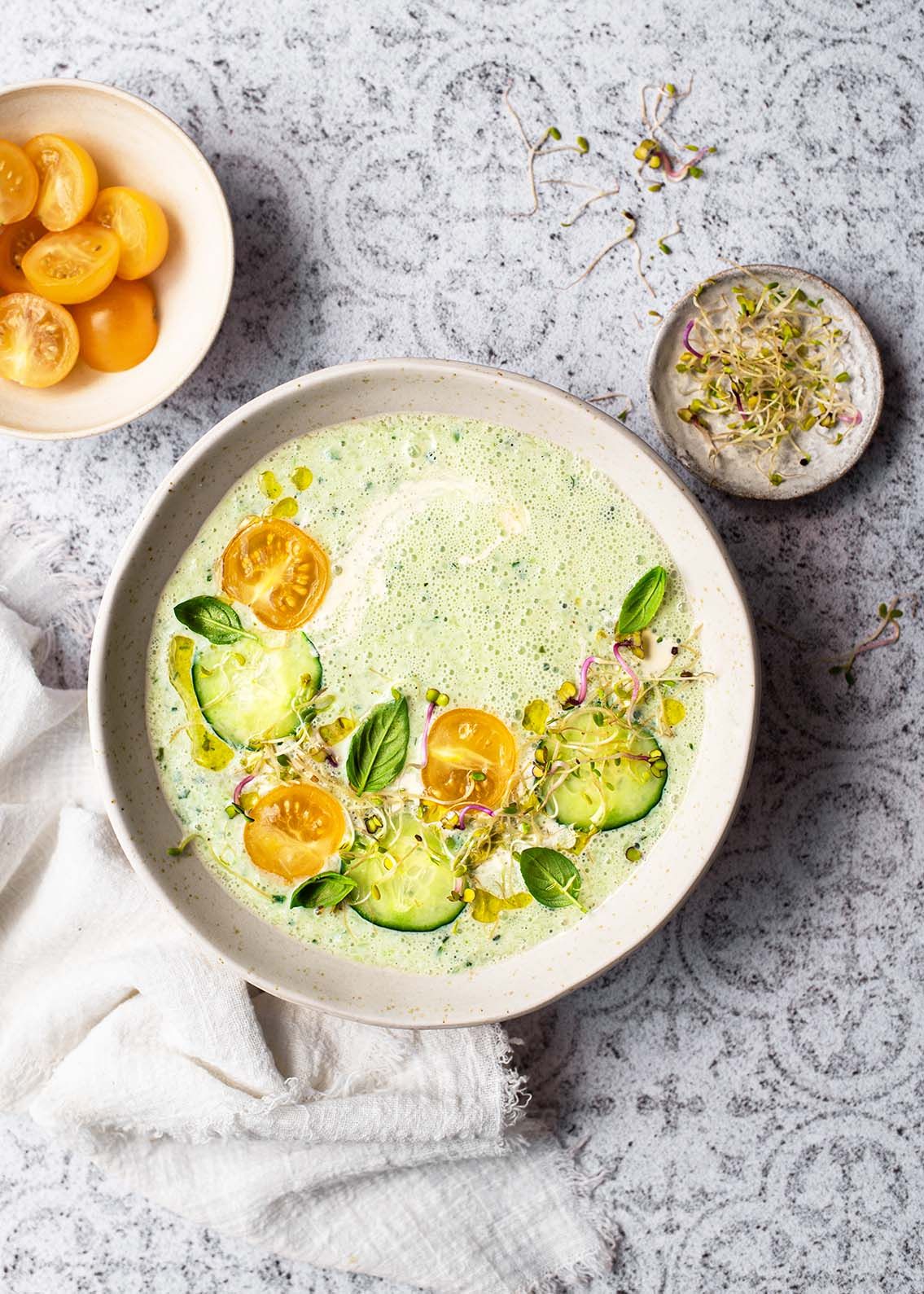Cold green soup garnished with cucumber slices and halved kumquats in a white bowl.