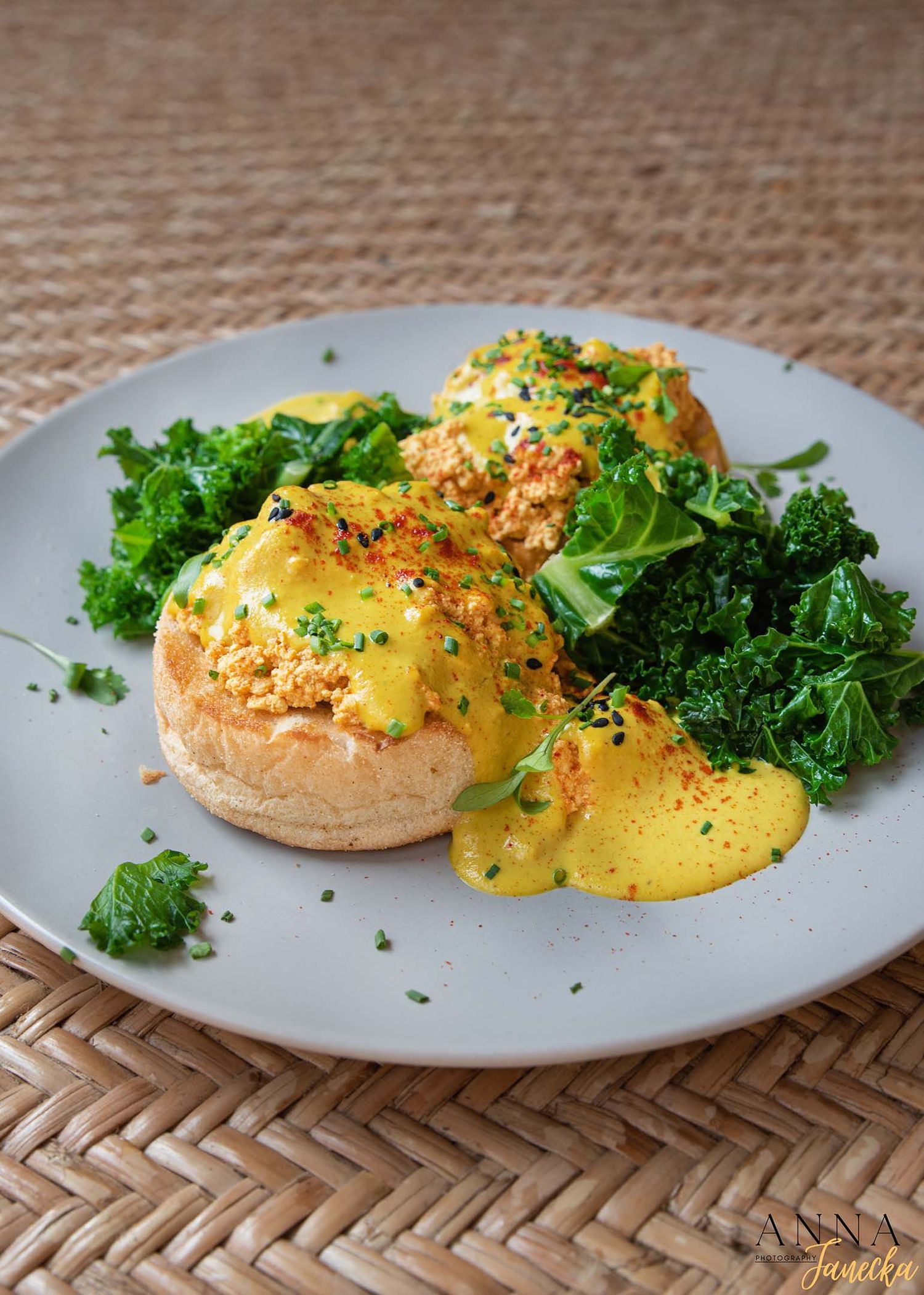 Eggs Benedict with hollandaise sauce and kale served on white plate with herbs.