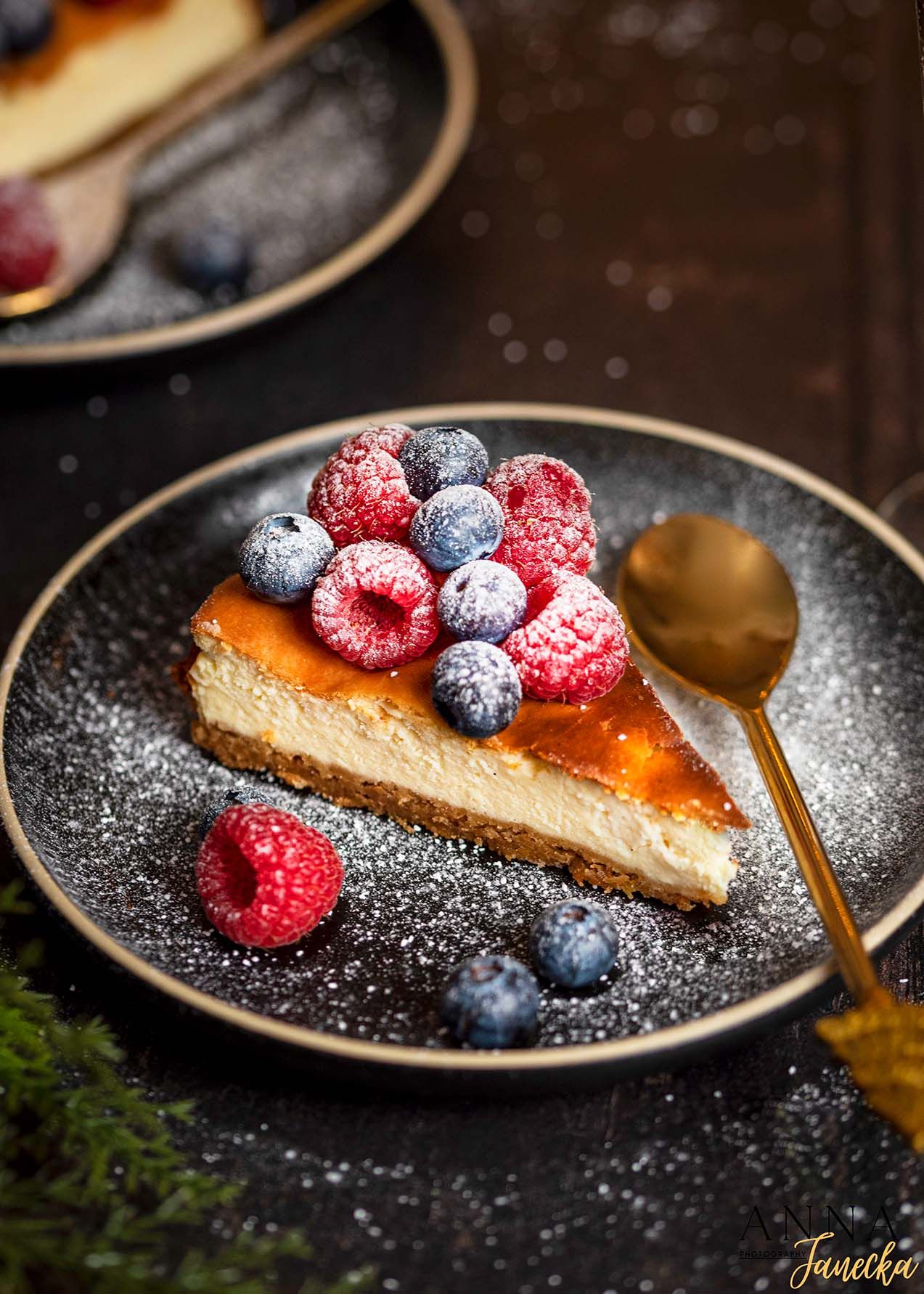 Cheesecake slice garnished with fresh berries and powdered sugar on a dark plate.